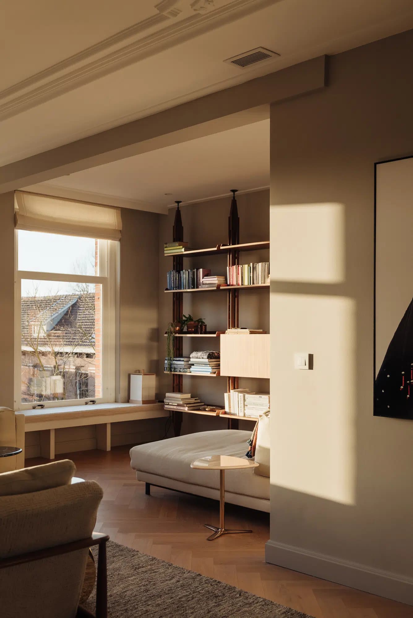 Woonkamer met houten tafel, bruine stoelen, groot raam en kunstwerk