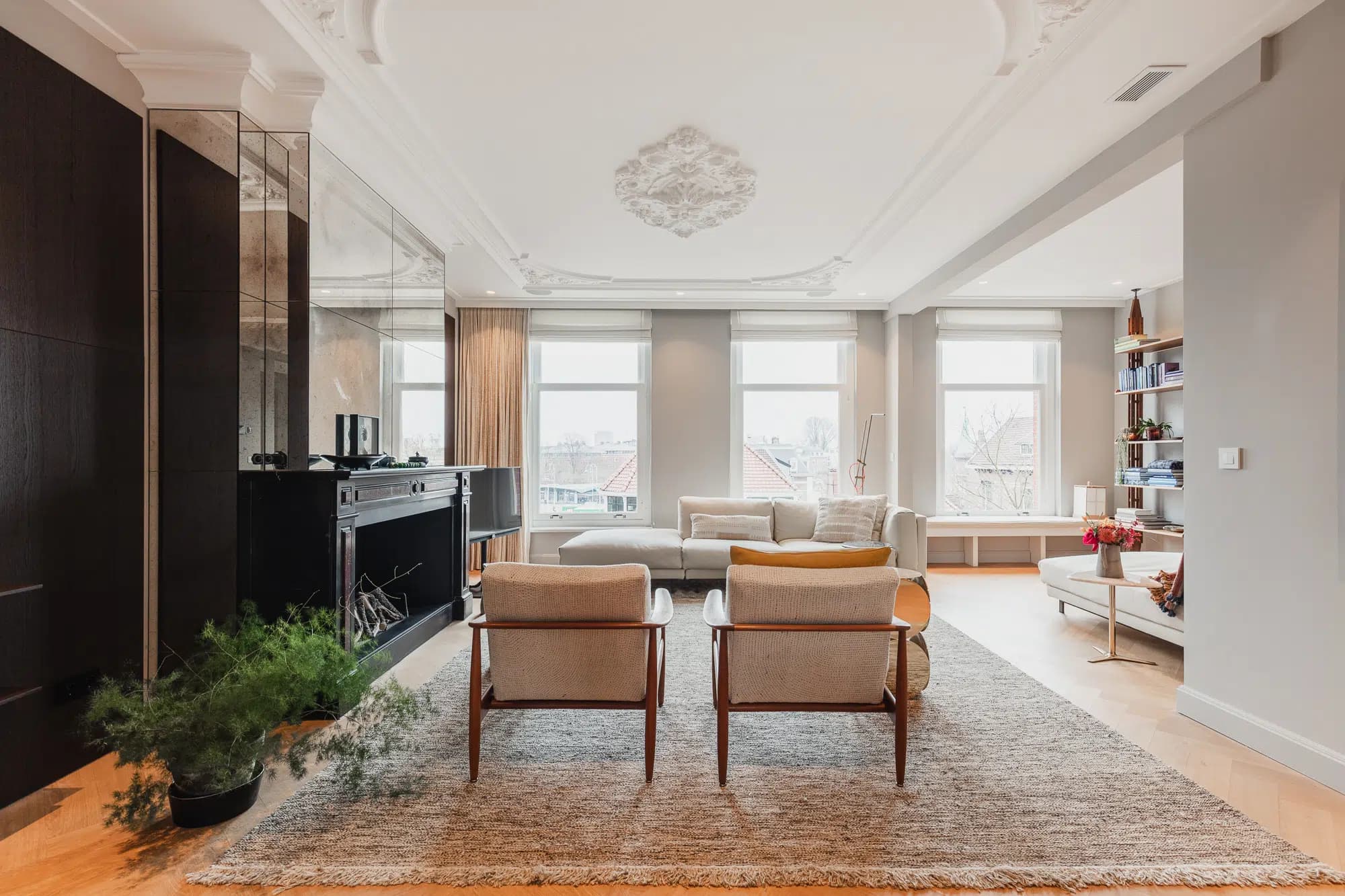 Grote woonkamer met open haard, houten fauteuils en brede daglicht