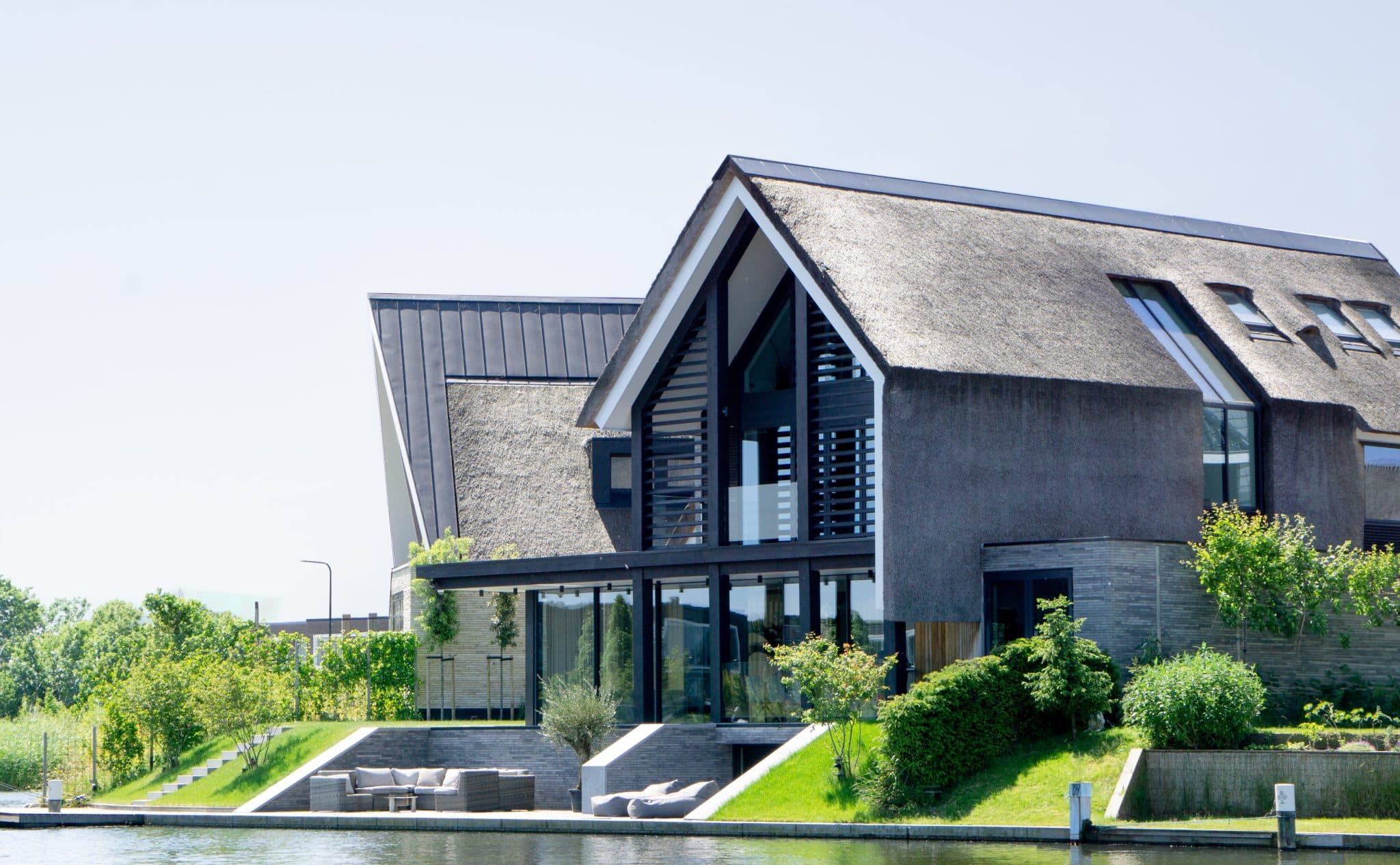 Moderne villa met rietdak, donkere voorgevel en groene tuinen aan water