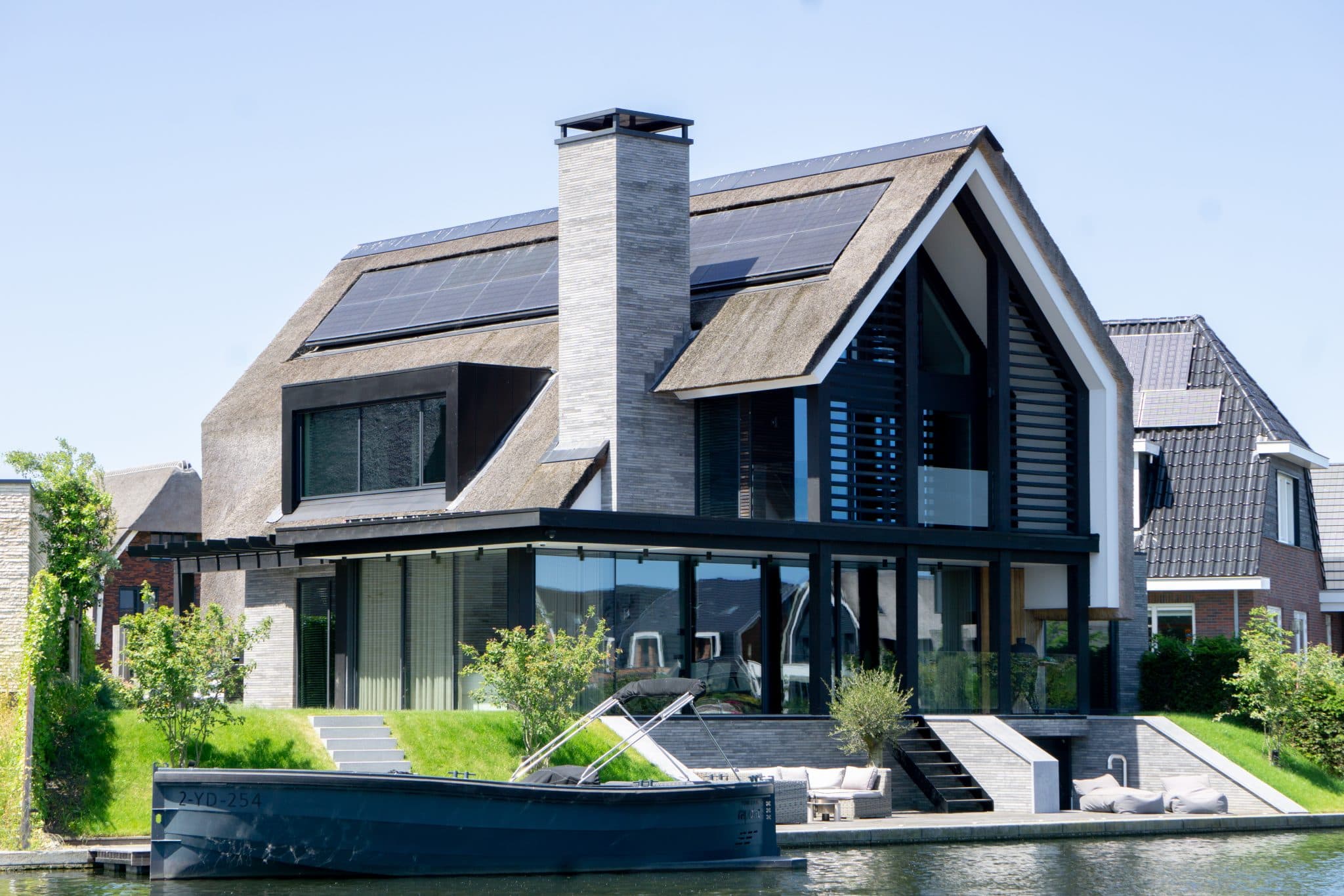 Moderne villa met rietdak, donkere houten frames en zwarte trap naar water