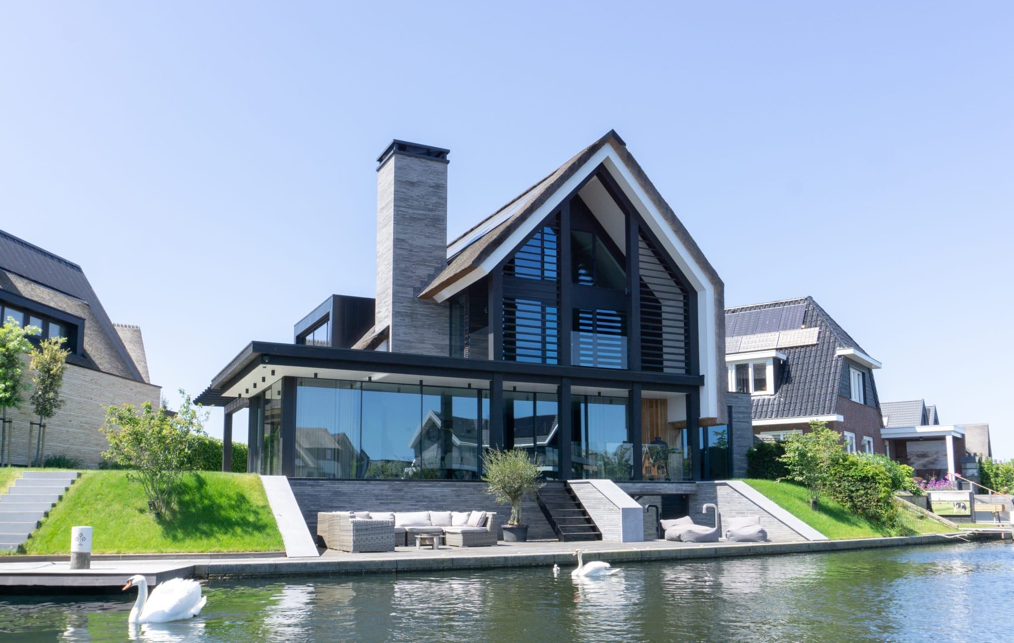 Moderne villa aan water met rietdak, grote glazen voorgevel en groene hellingen