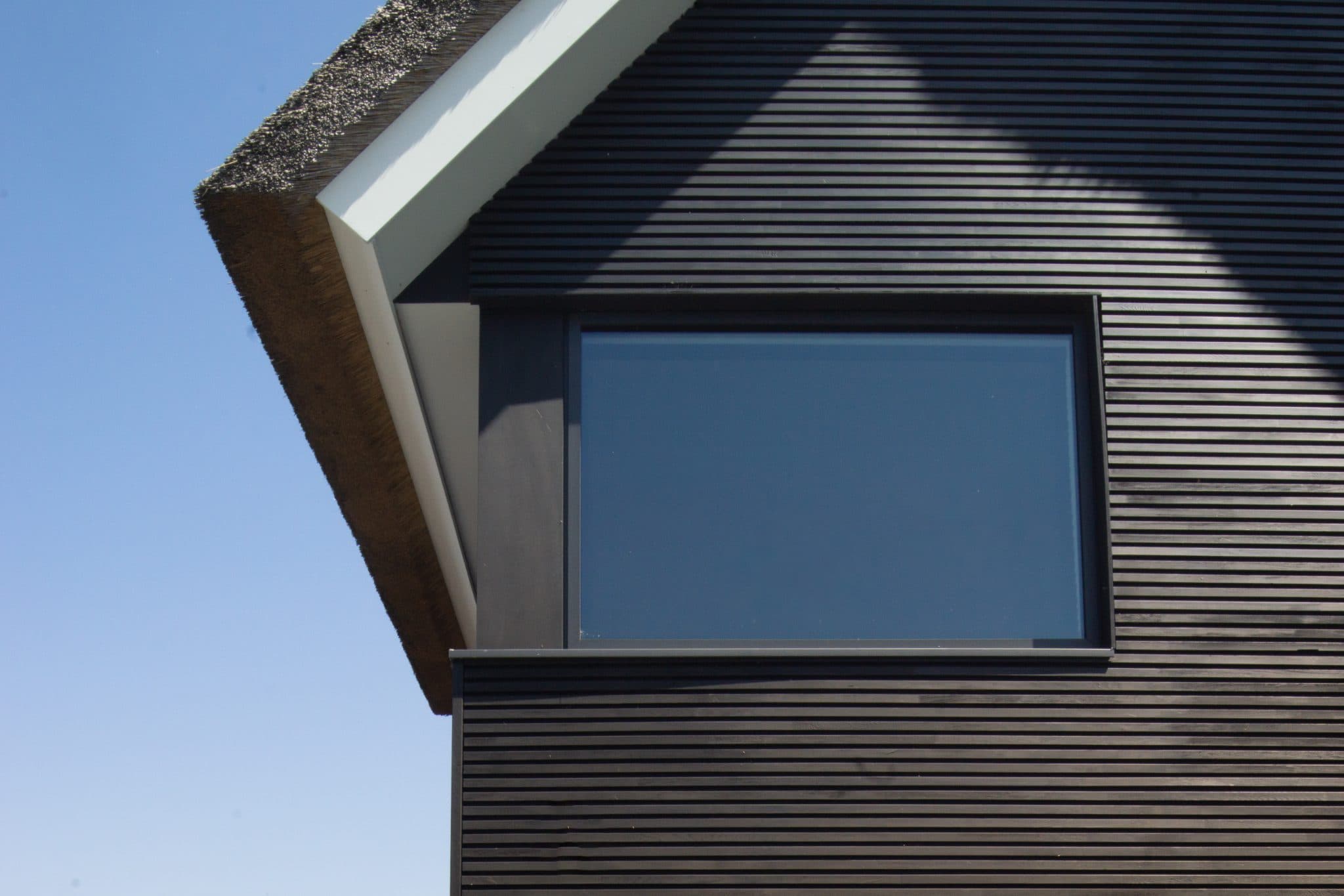 Donkere ribbelwand villa met rietdak en prominent raam in spitse gevel