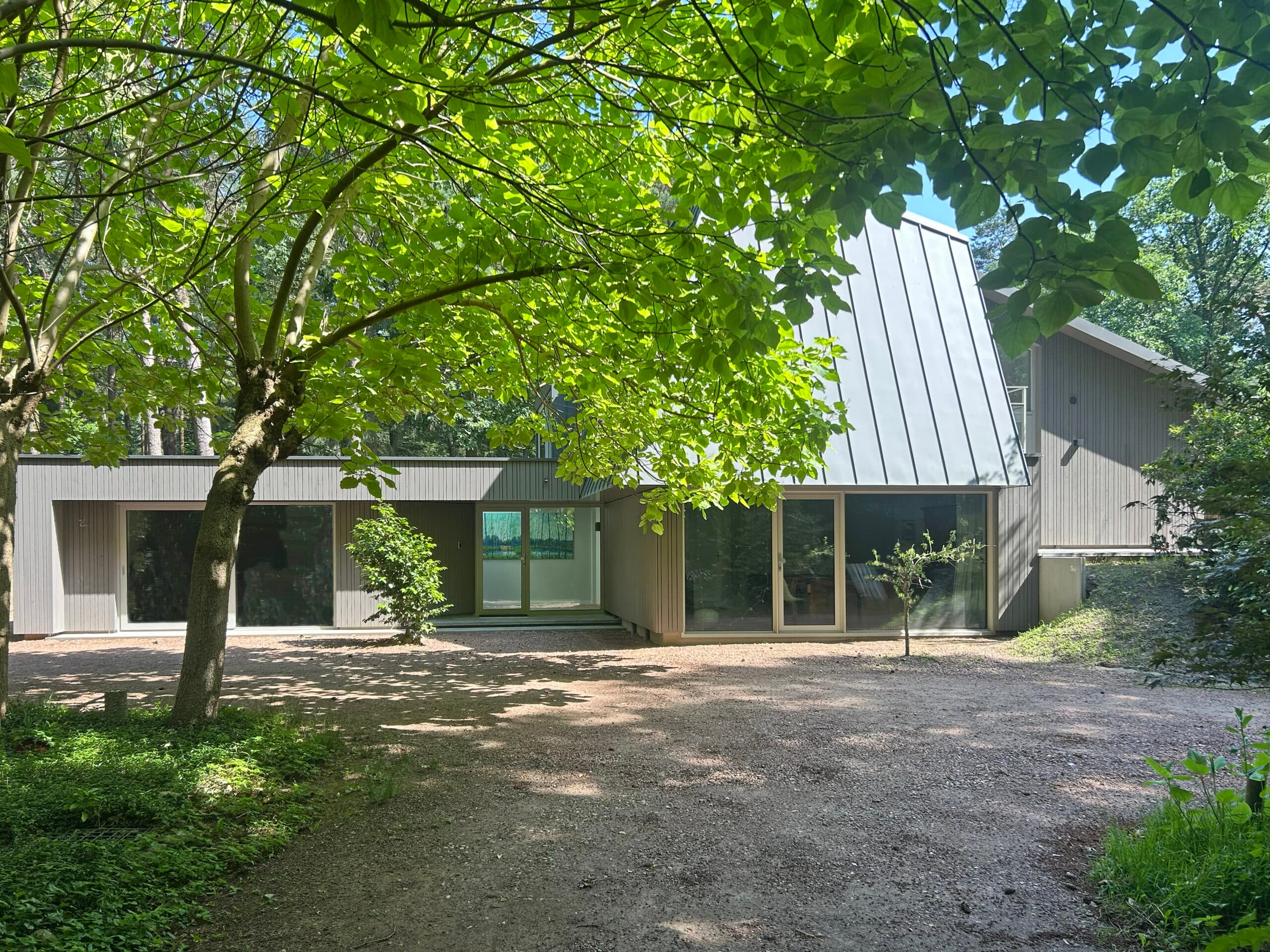 Voorgevel villa met witte golfplaten, grote ramen, grindpad