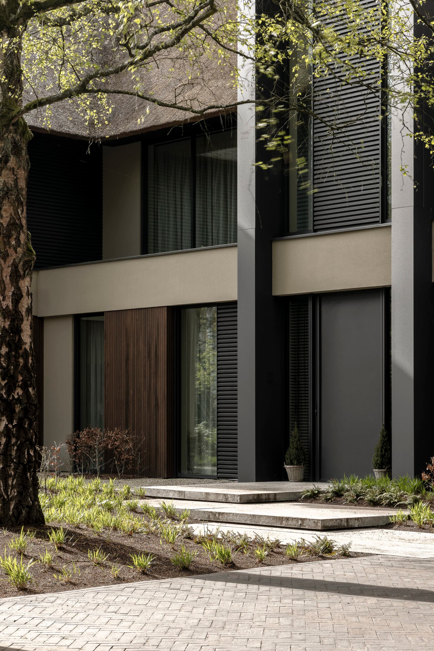 Ingang moderne woning met zwarte luiken, beige zijwand en trapreden