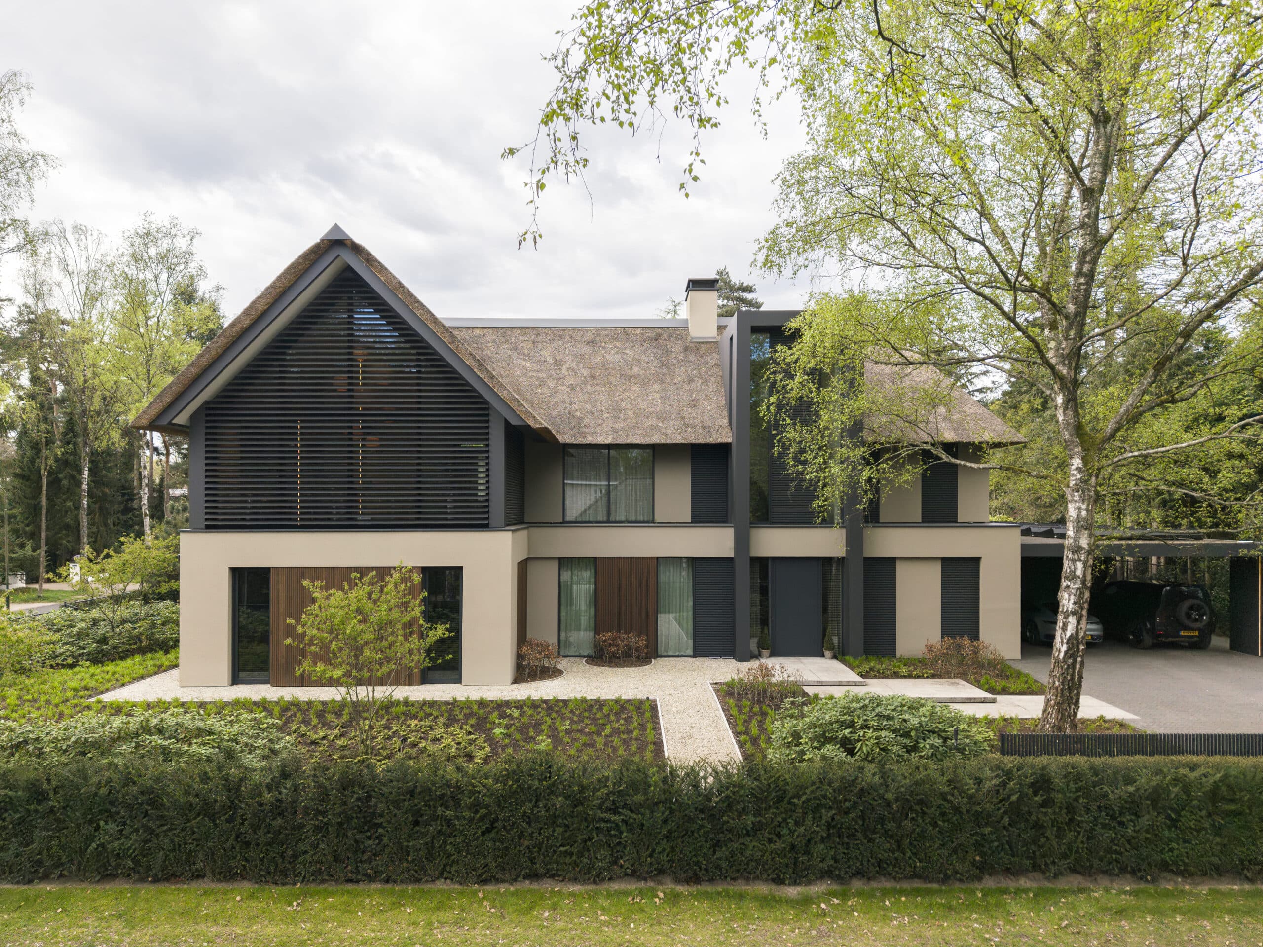 Voorgevel villa met zwarte lamellen, beige zijwanden en rieten dak