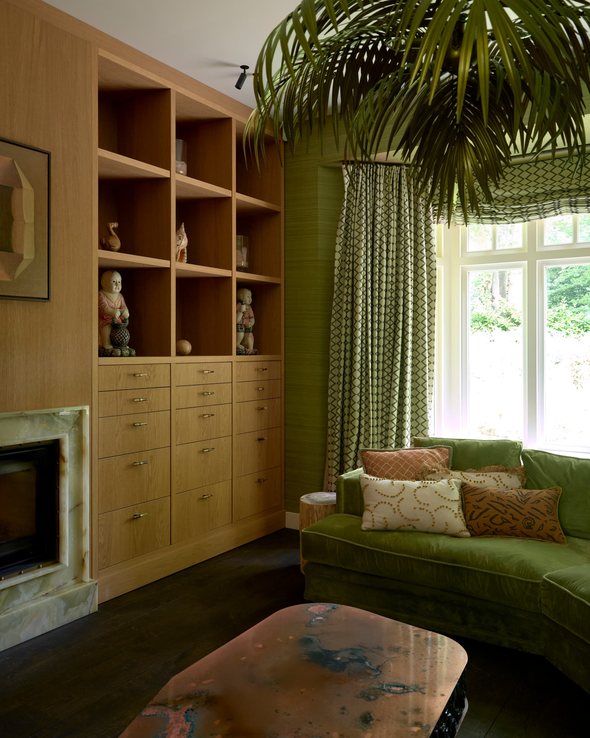 Zithoek met groene fluweelsofa en houten kastenwand met open vakken