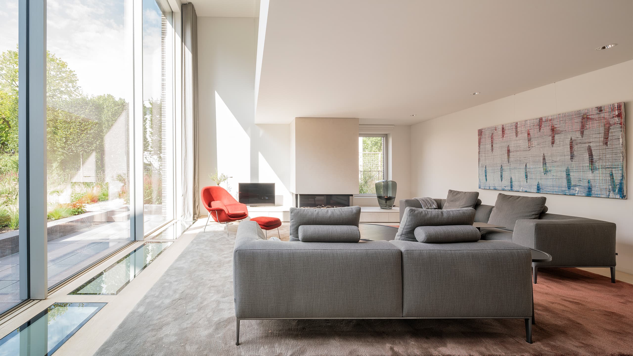 Minimalistisch woonkamer met grijze banken, rood accent-fauteuil en grote ramen