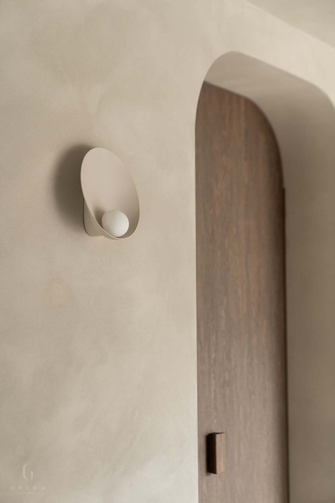 Detailopname witte muur met ovale nislamp en donkebruine deur
