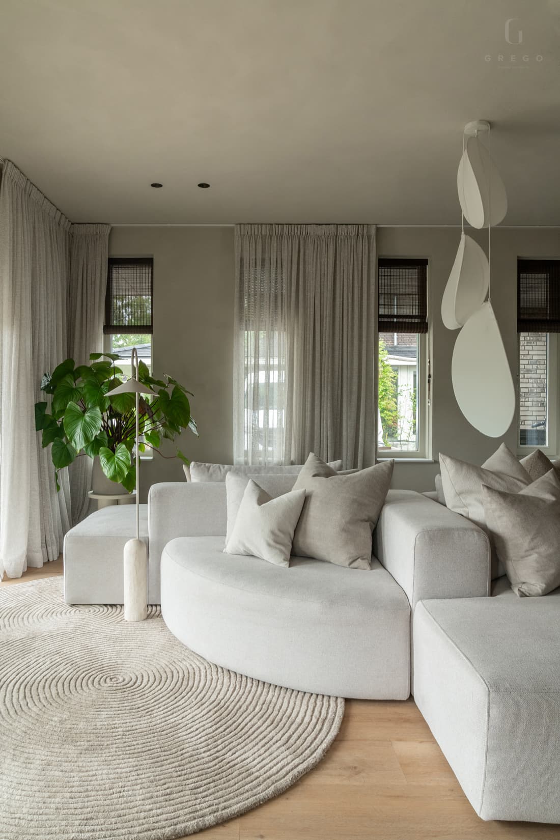 Woonkamer met beige hoekbank, ronde tapijt en twee hangende lampen