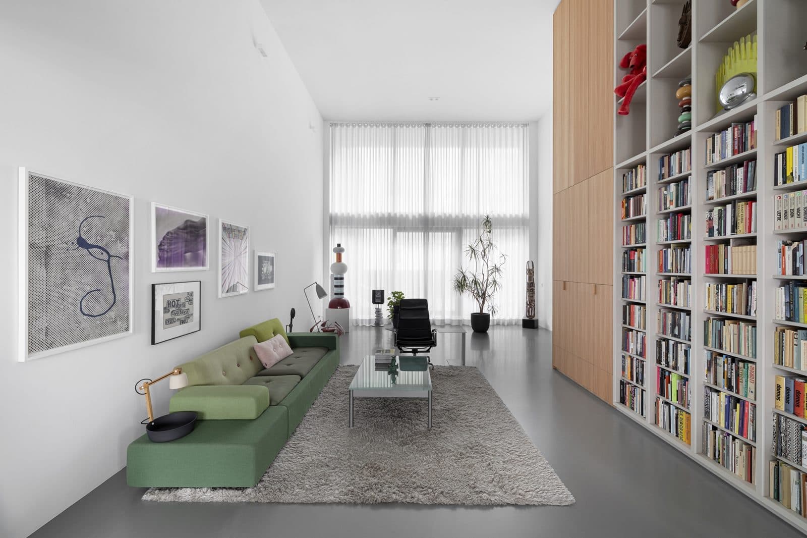 Woonkamer met groene bank, grijze vloer en boekenkasten