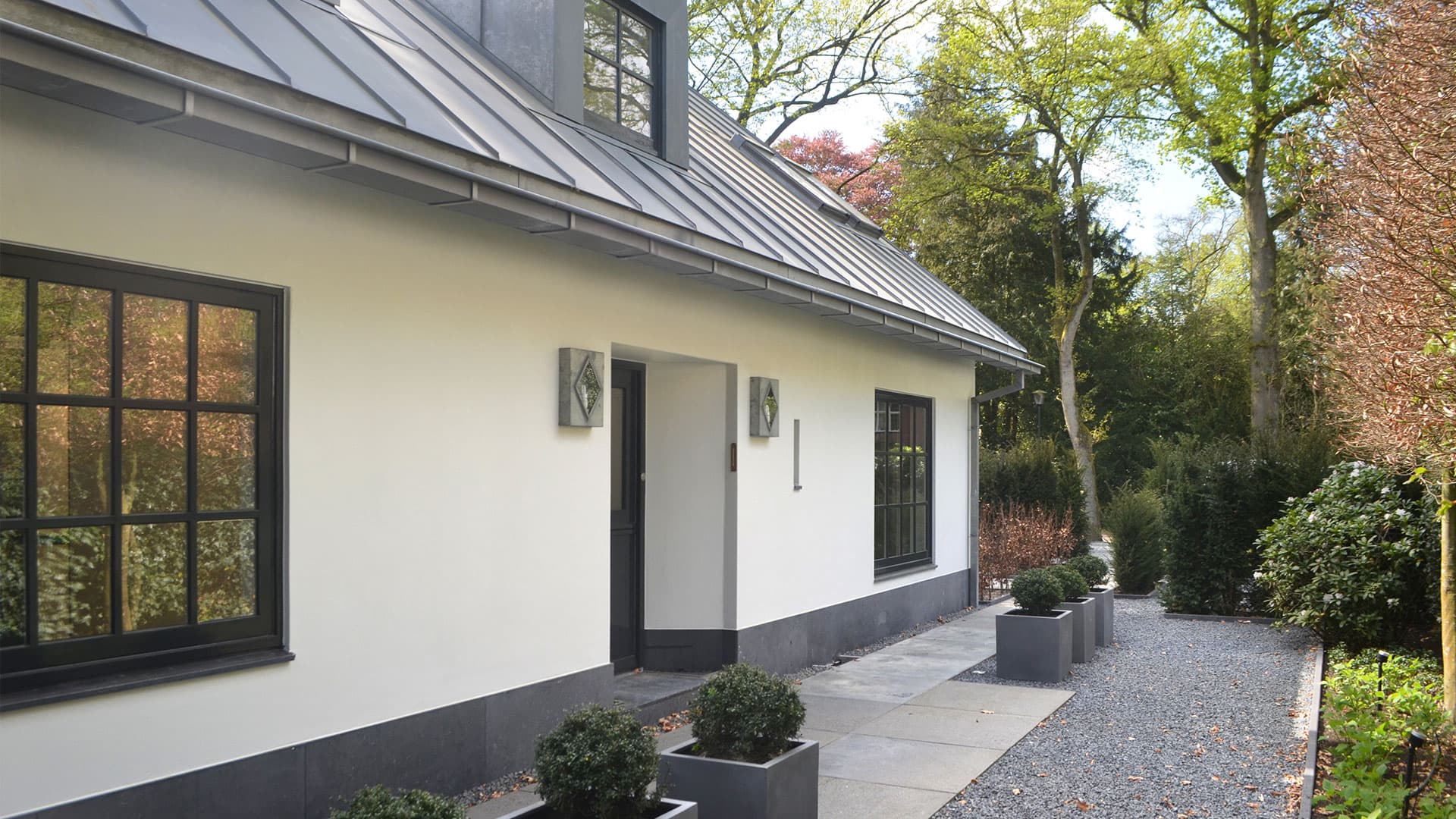 Witte villa met zwarte daklijsten, stalen ramen en grindpad