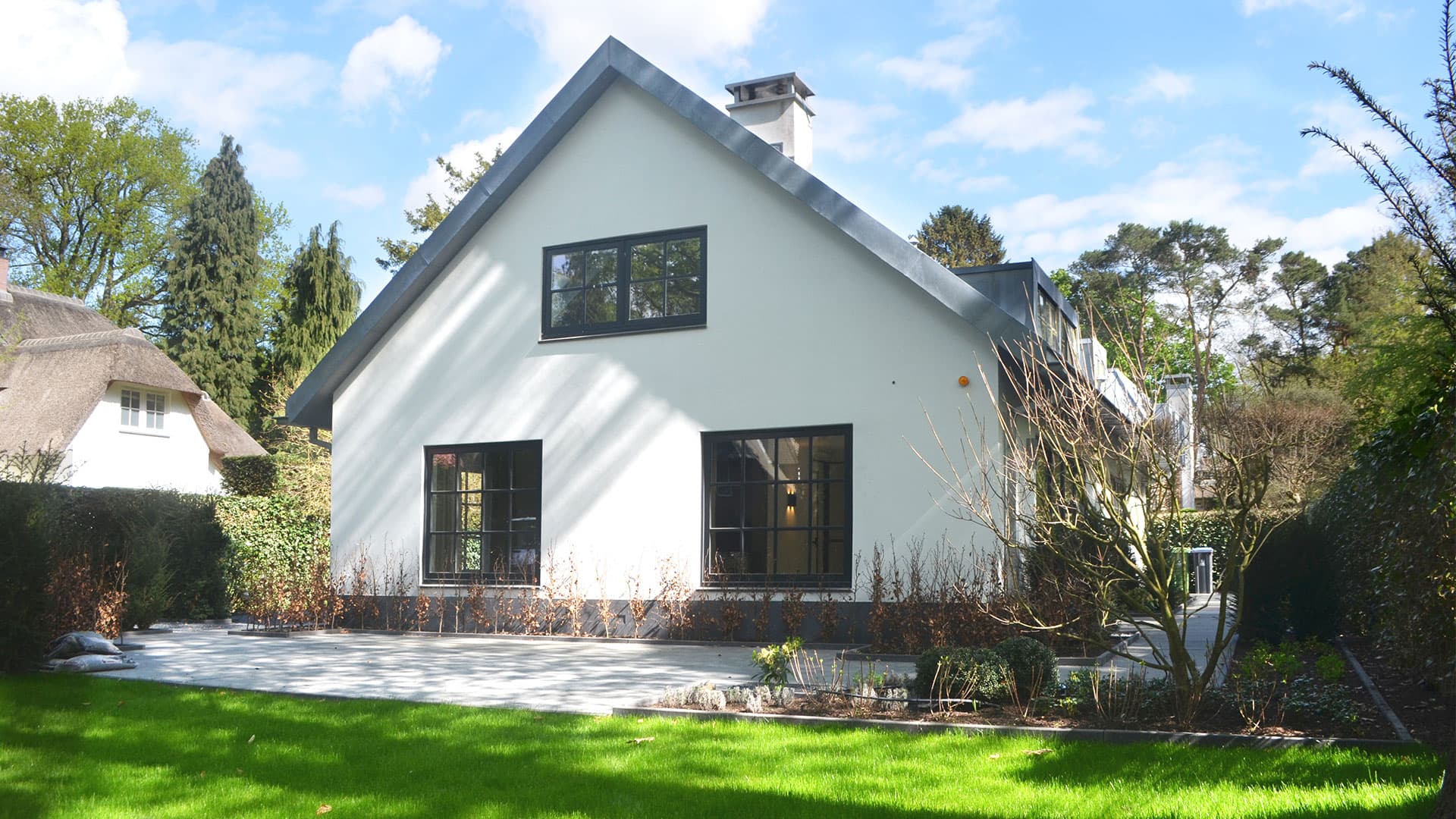 Modern witte villa met donkere ramen, hellend dak en terrasplaten