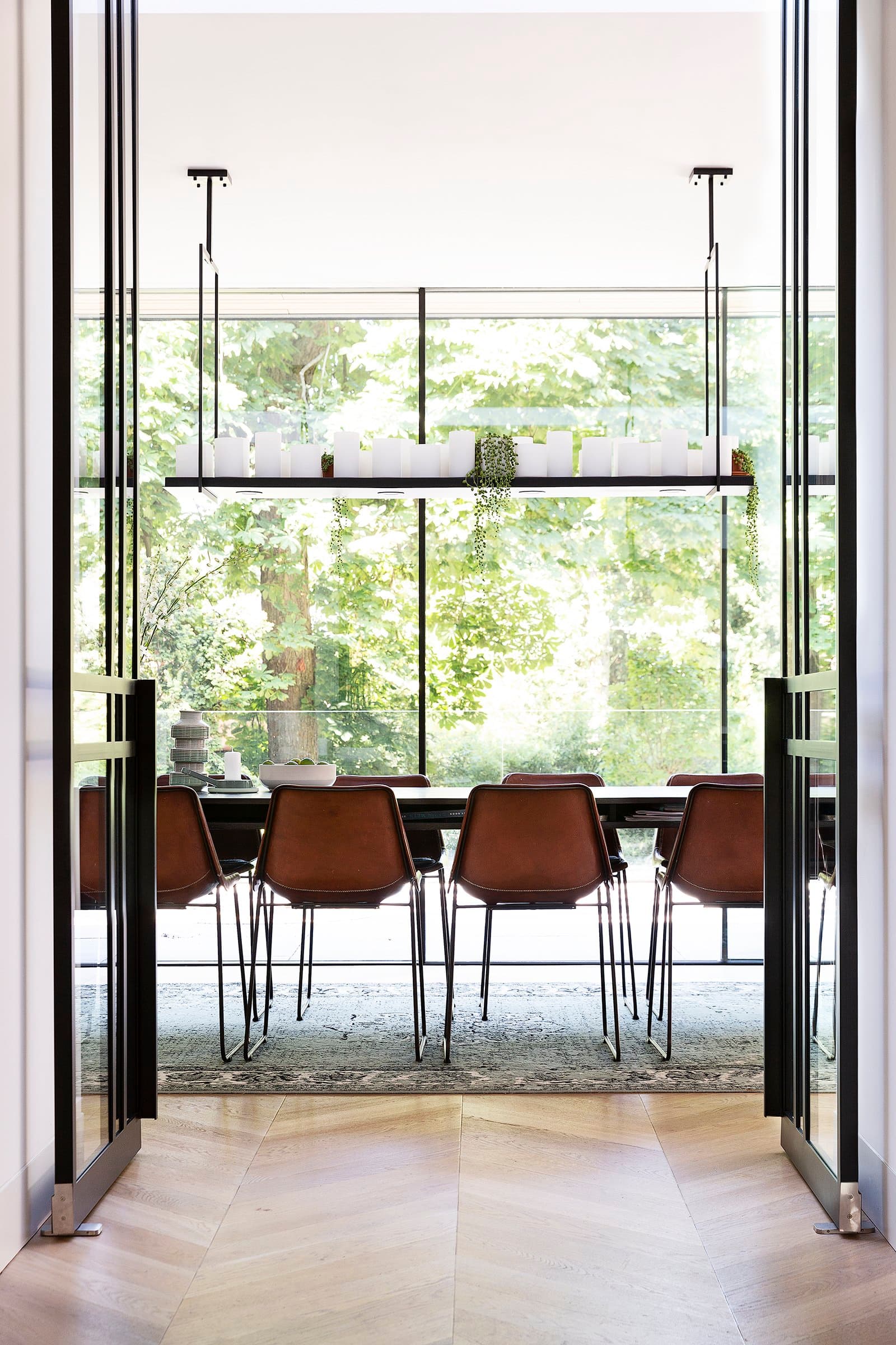 Eettafel met bruine leren stoelen, grote raamwand op bos uitzicht