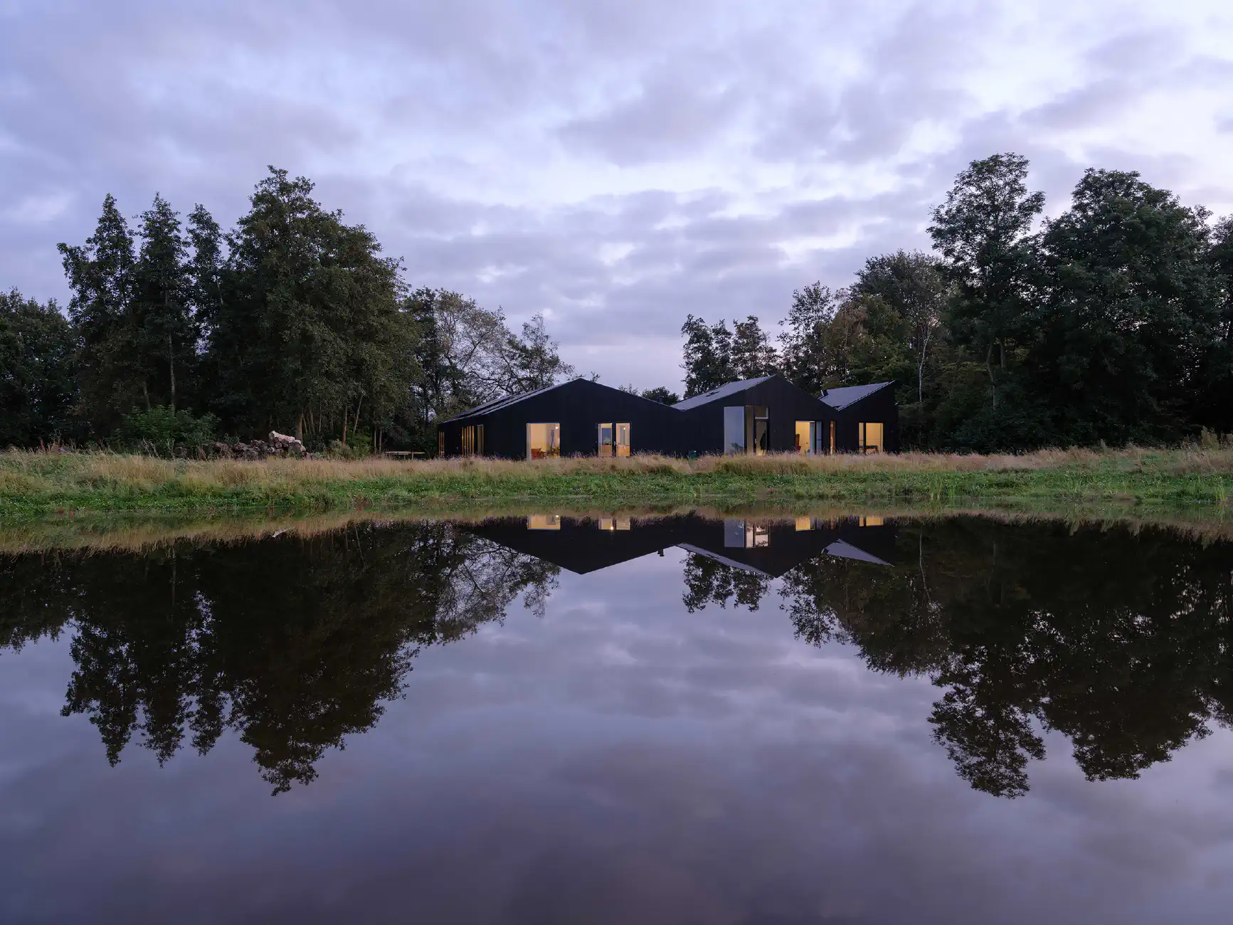 Zwart huis met ramen gereflecteerd in vijver bij schemering