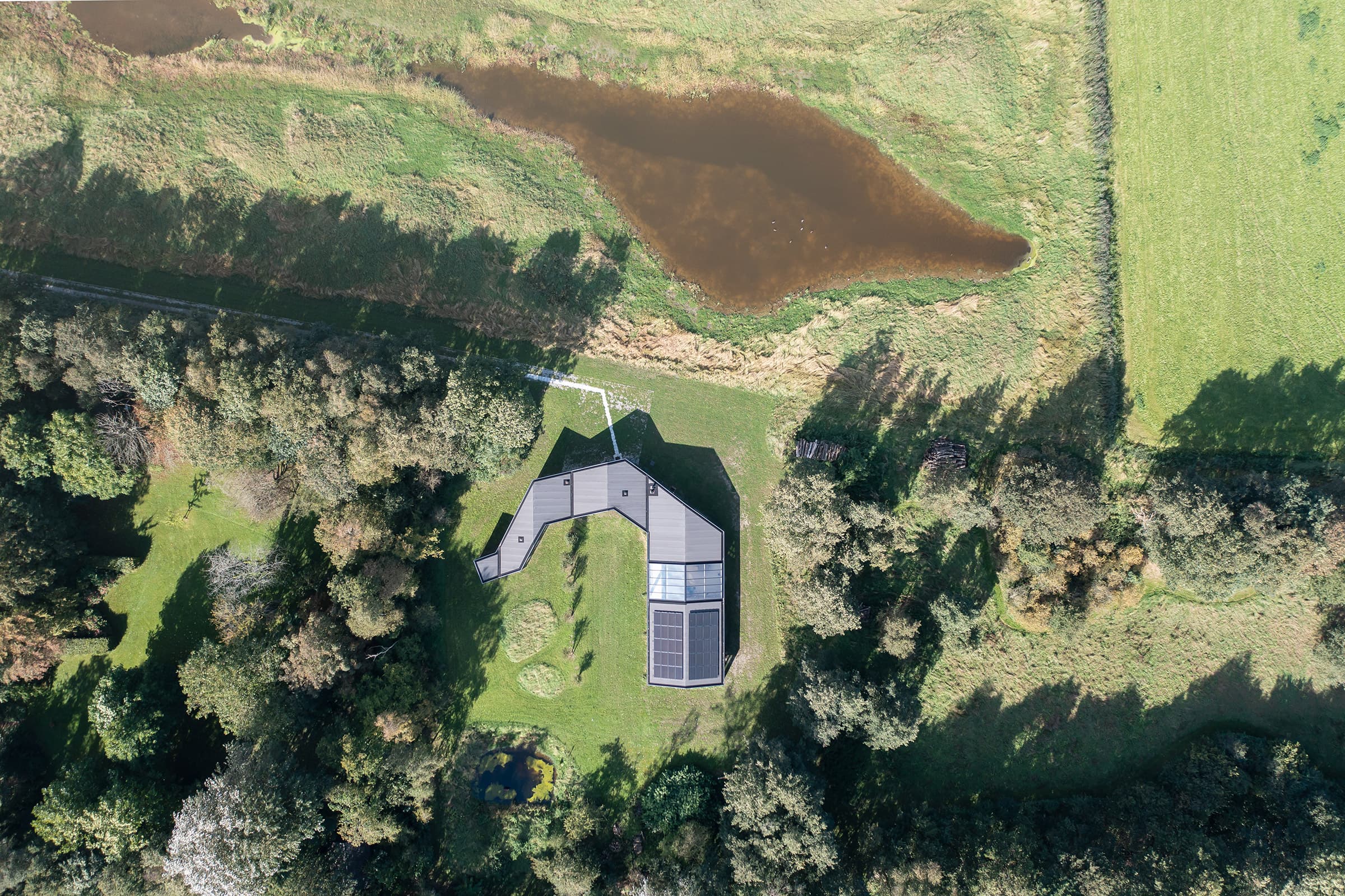 Luchtfoto zwart huis met zonnepanelen omgeven door bomen en weiden