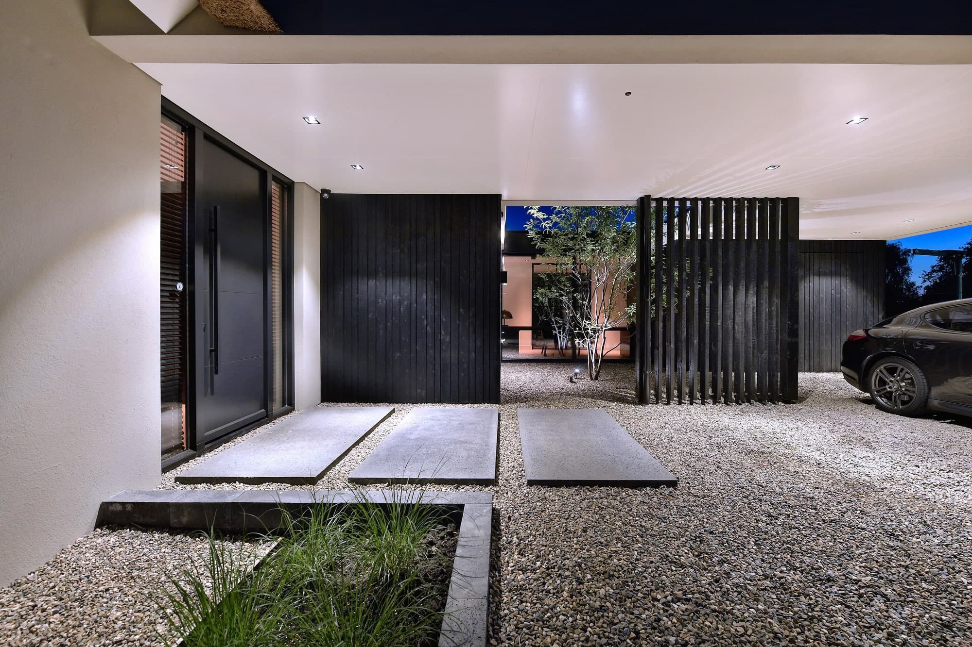 Carport met zwart stalen poort, grind en betonnen traptreden