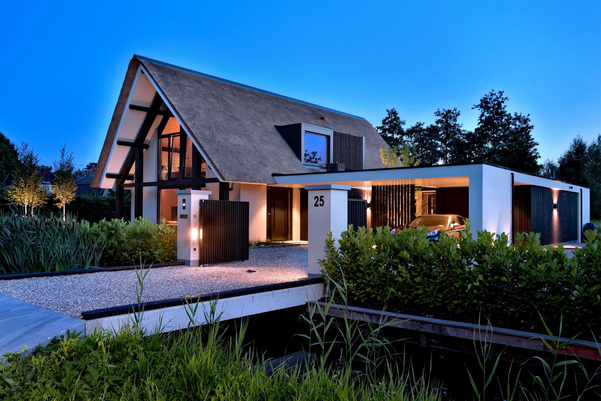 Villa met pannendak, witte gevel, zwart spanten en waterpartij bij avond