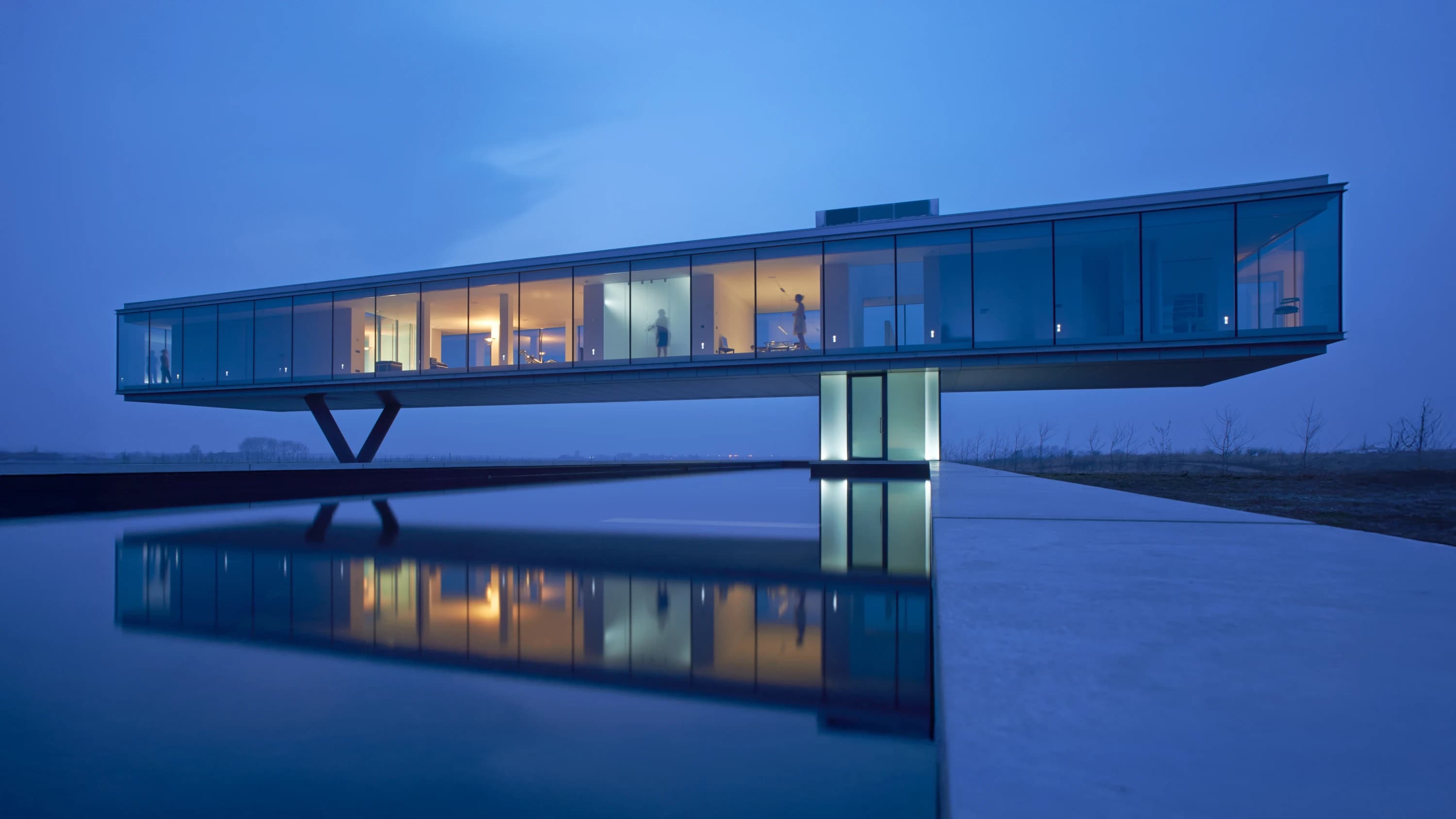 Moderne villa met glazen gevel en V-vormige betonnen zuilen, waterspiegeling