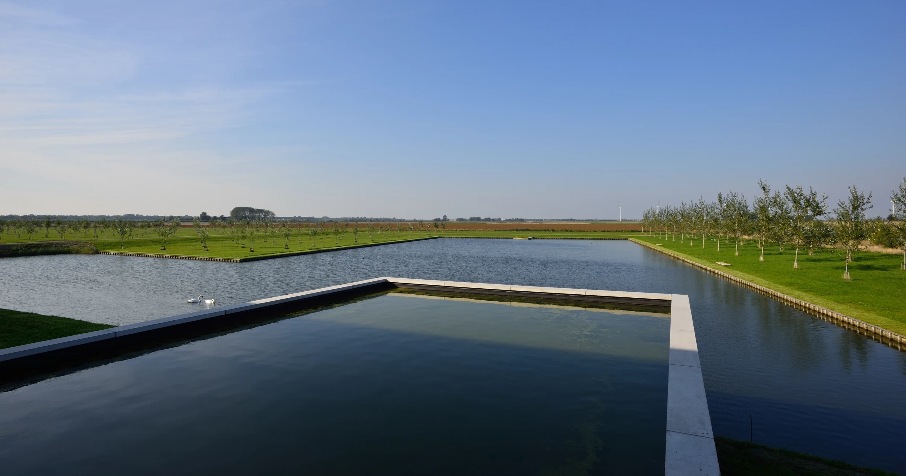 Moderne villa met glas en zwart profiel naast waterpartij op landelijk terrein