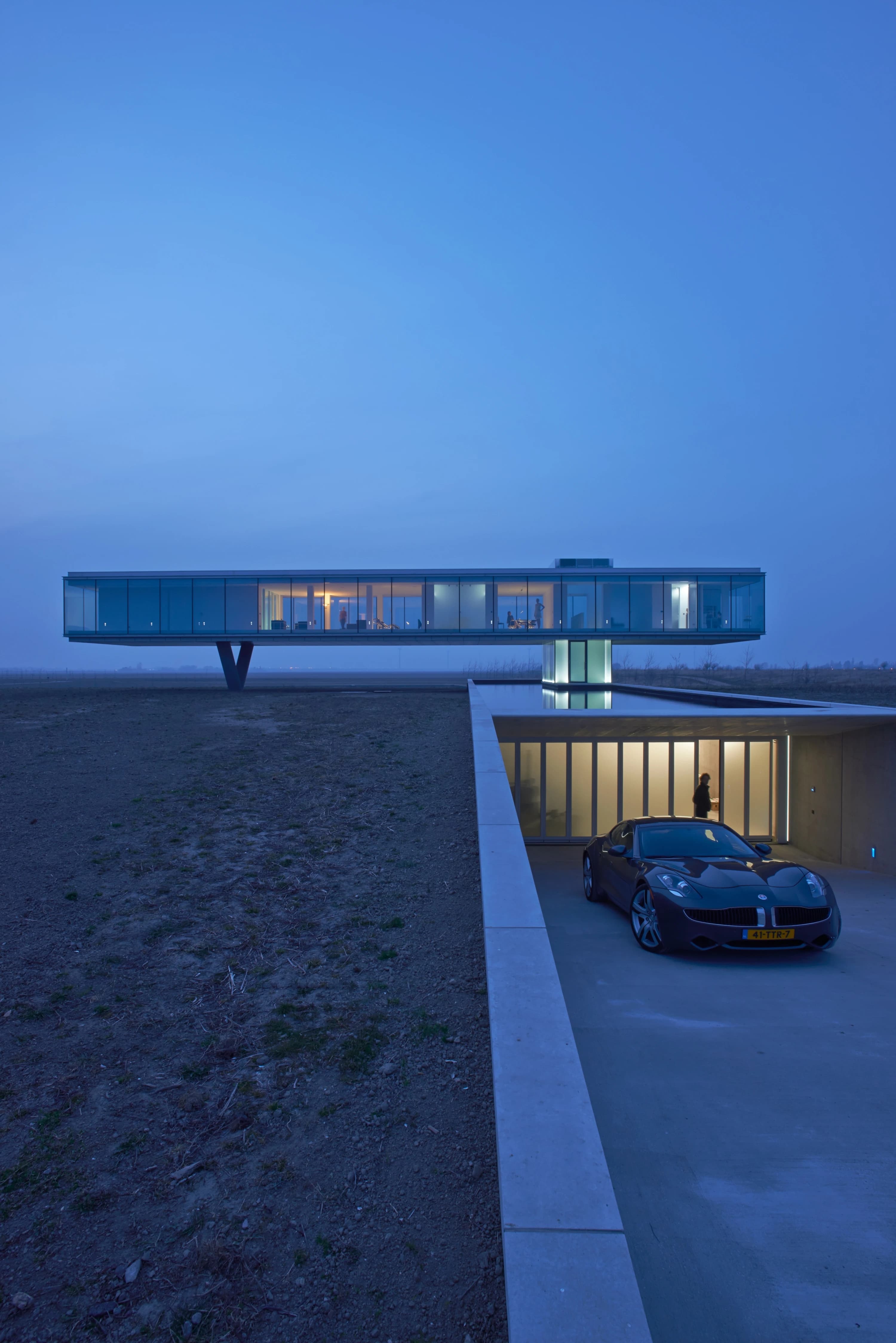 Moderne villa met glazen gevel, betonnen zuil en ondergrondse garage met auto