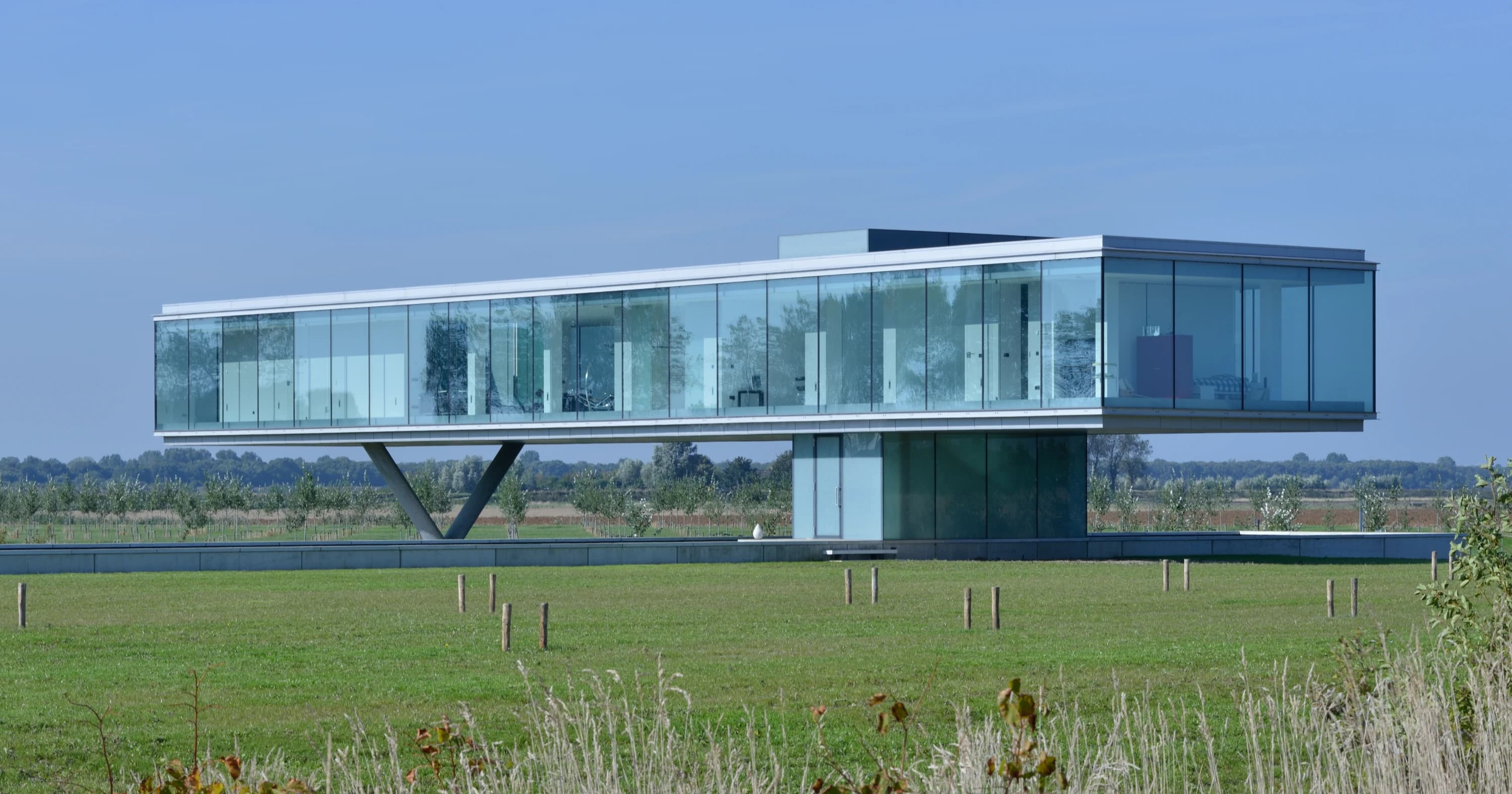Moderne villa met glazen gevel en V-vormige betonnen steun, landschapszetting