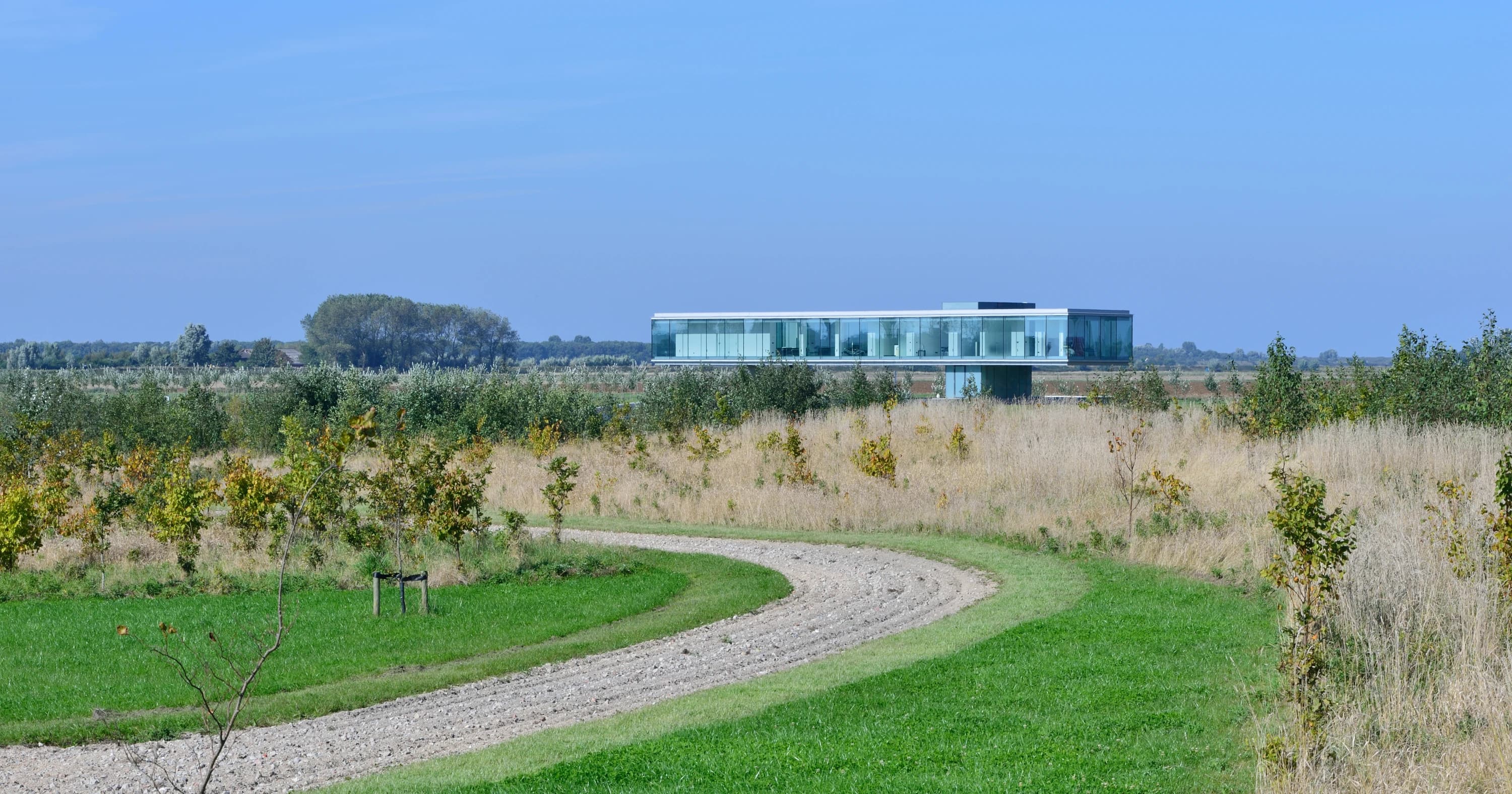 Moderne villa met glazen gevel aan rand van weiland, kronkelende oprit