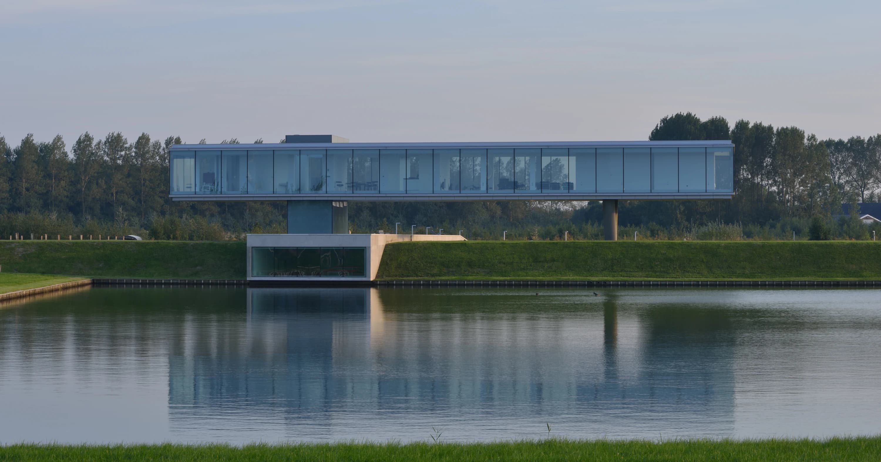 Moderne villa met glazen gevel en betonnen support, reflectie in waterkanaal