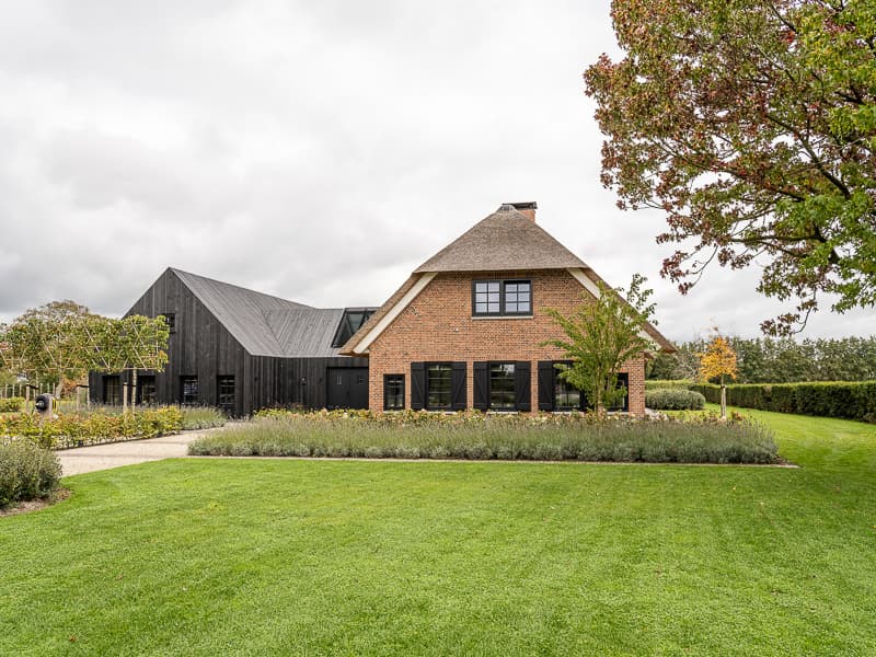 Rietgedekte villa met bakstenen gevel, zwarte ramen en gravel pad