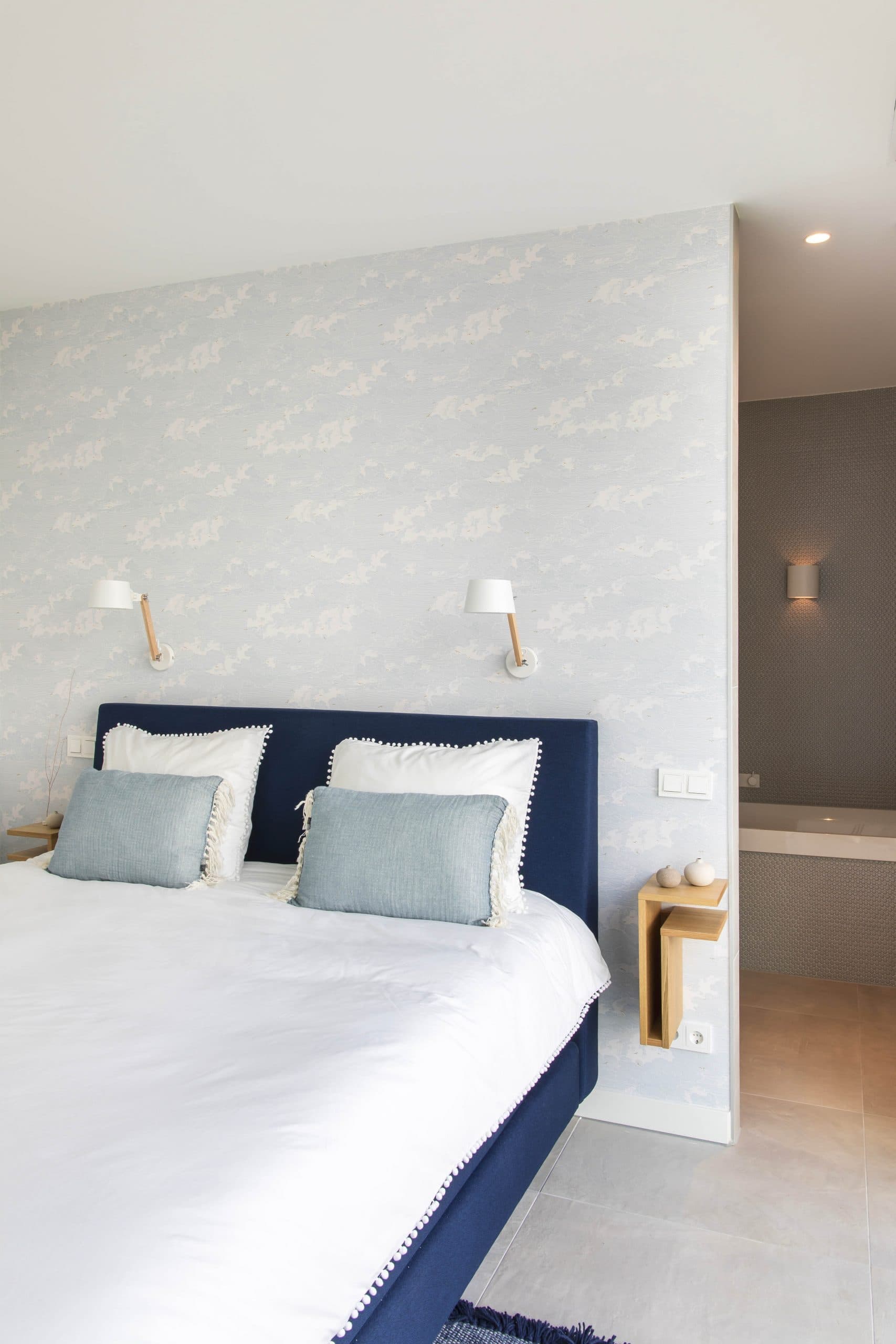 Slaapkamer hoofdeinde met witte wandbekleding, blauwe kader en wandlampen