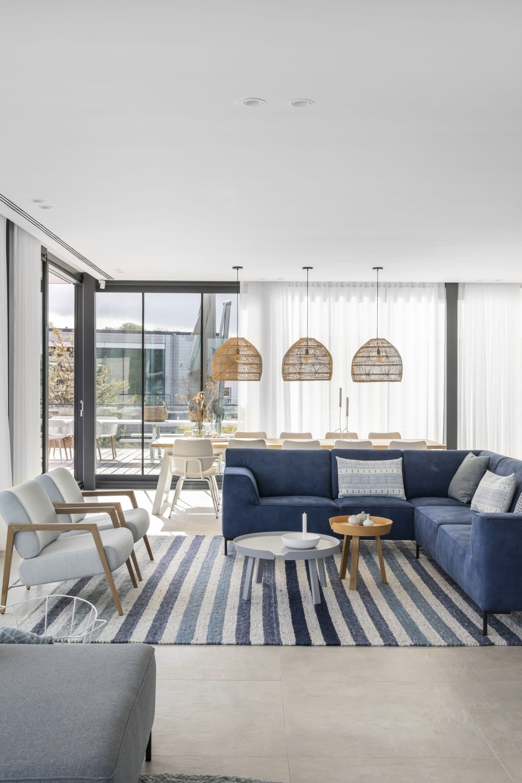Open woonkamer met donkerblauwe bank, rieten hanglamp en maritiem geïnspireerd interieur