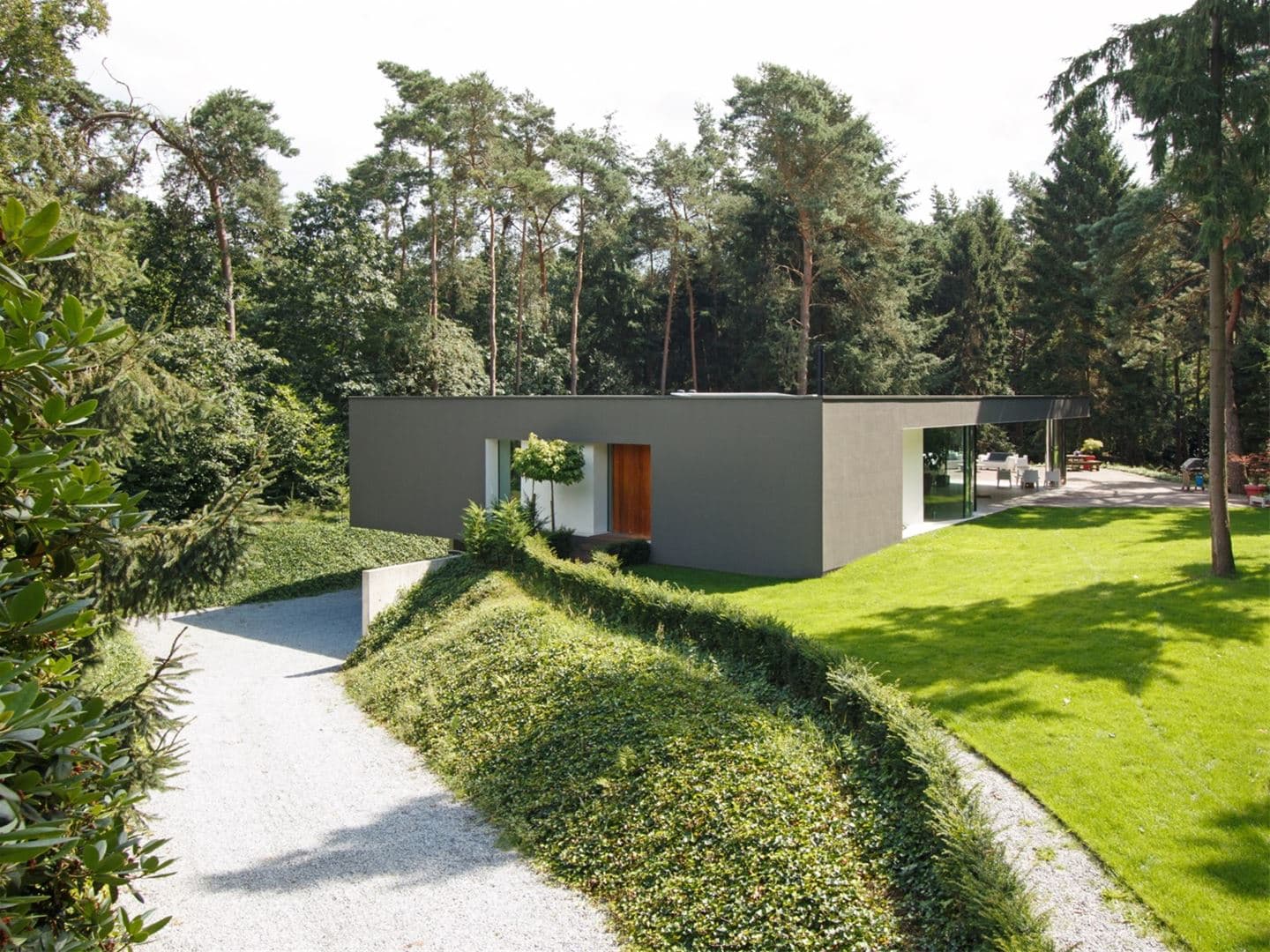 Voorkant villa met ingang en grasveld omgeven door bomen