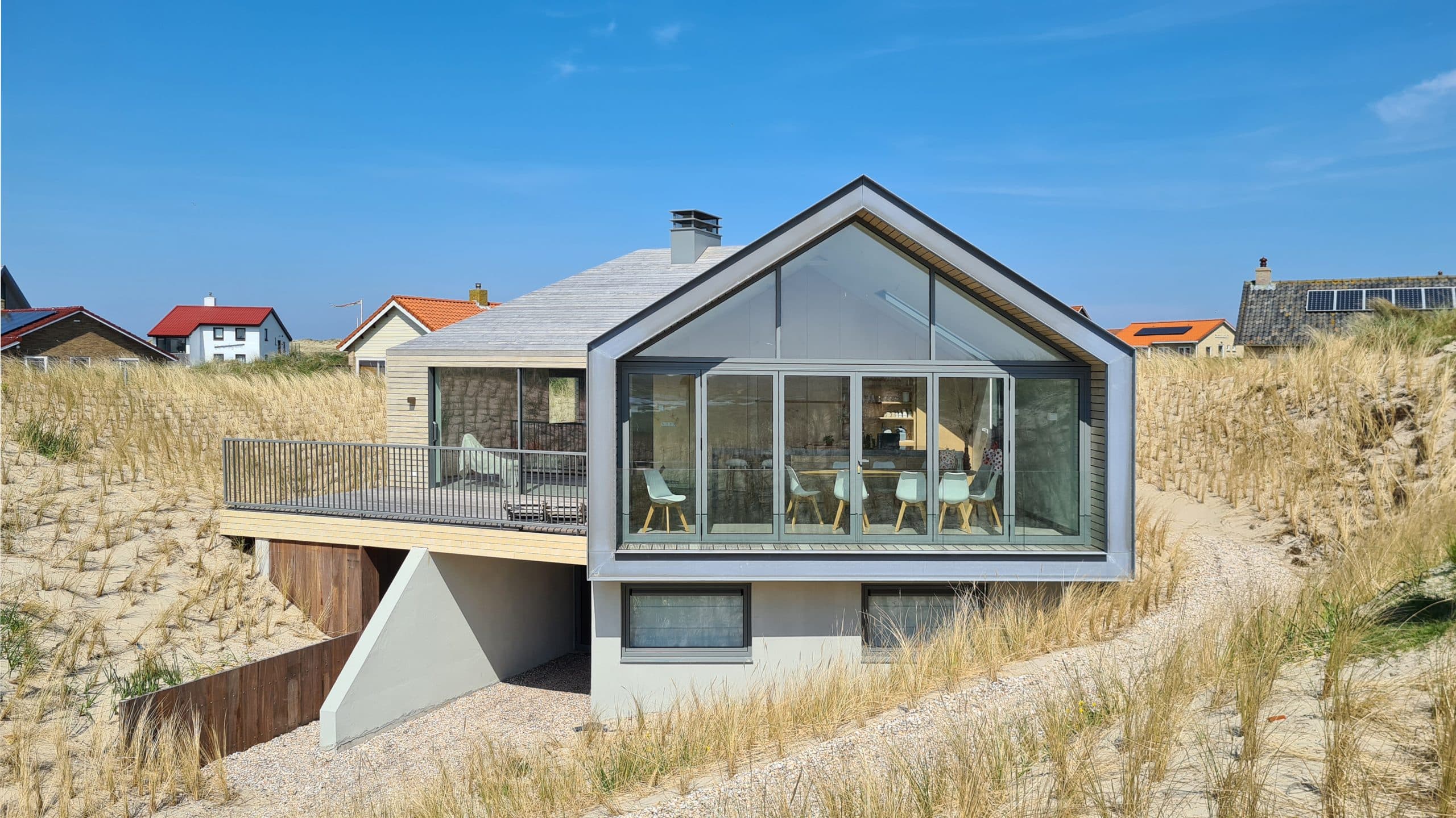 Moderna villa met grijze gevelbekleding en grote raampartijen tegen zandduinen