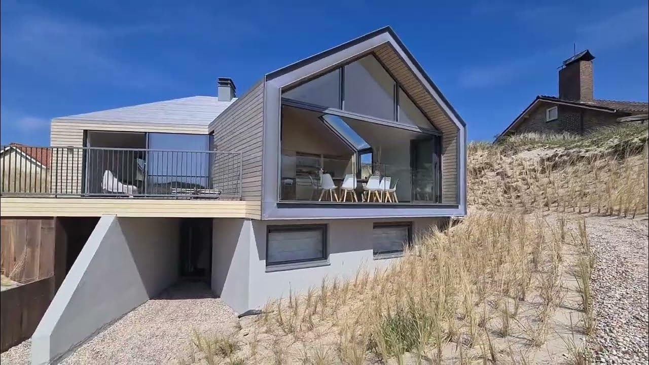 Villa op palen met grijze houten bekleding en witte betonnen onderbouw