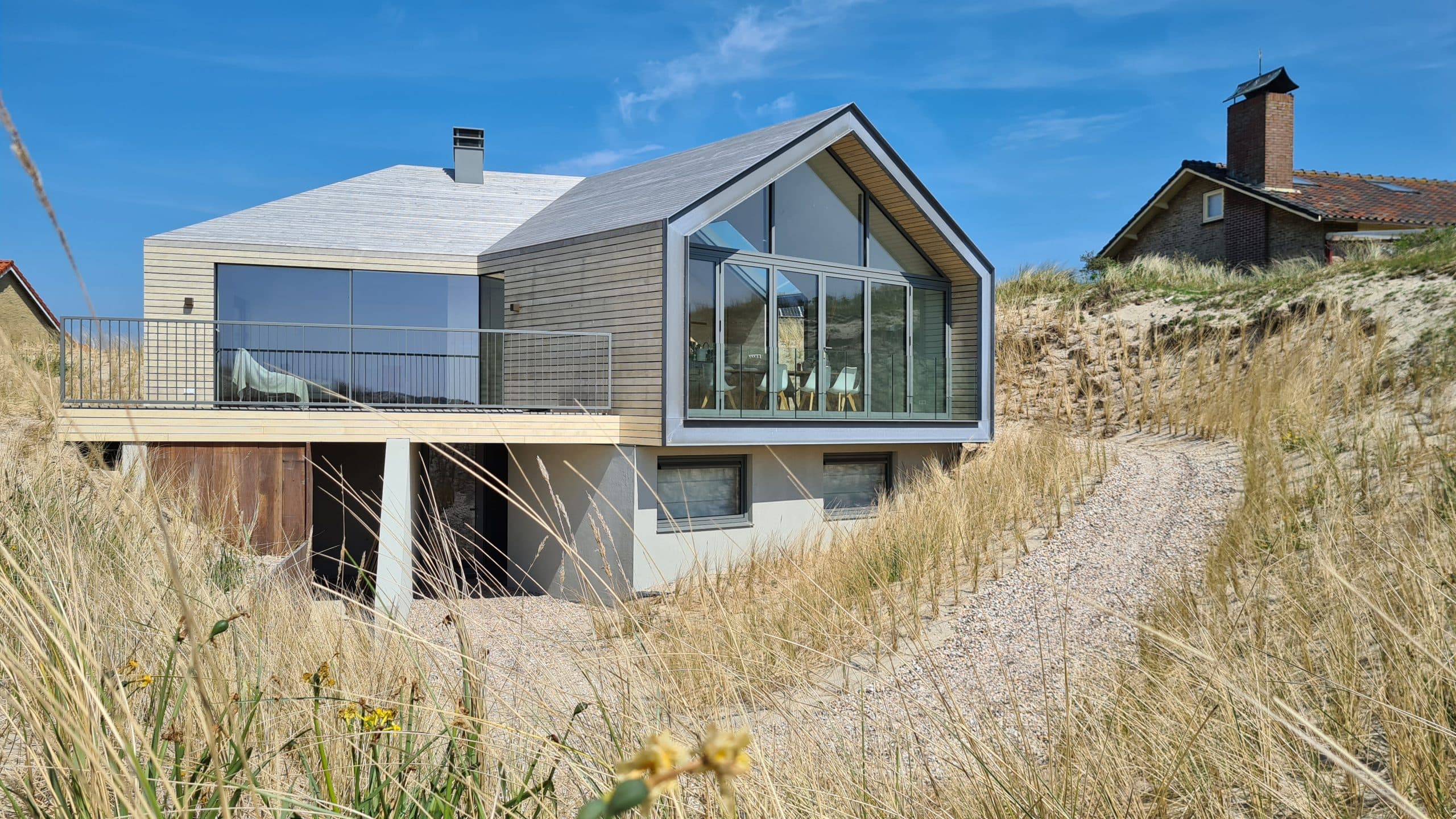 Villa op palen met wit beton en grijze houten zijgevels in duinlandschap