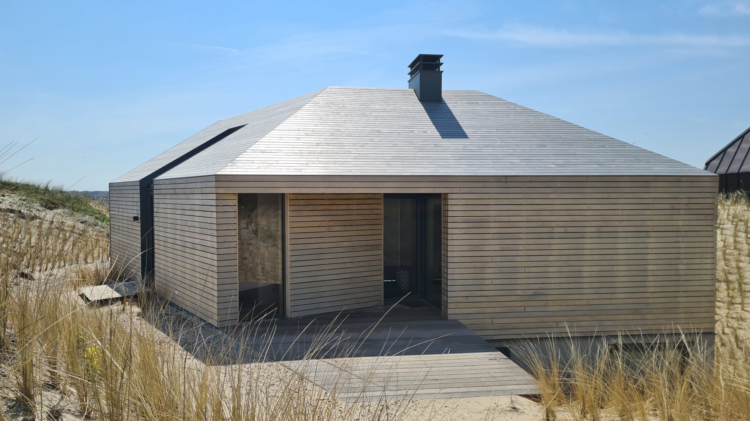 Moderne villa met grijze houten bekleding en houten terras aan duinrand