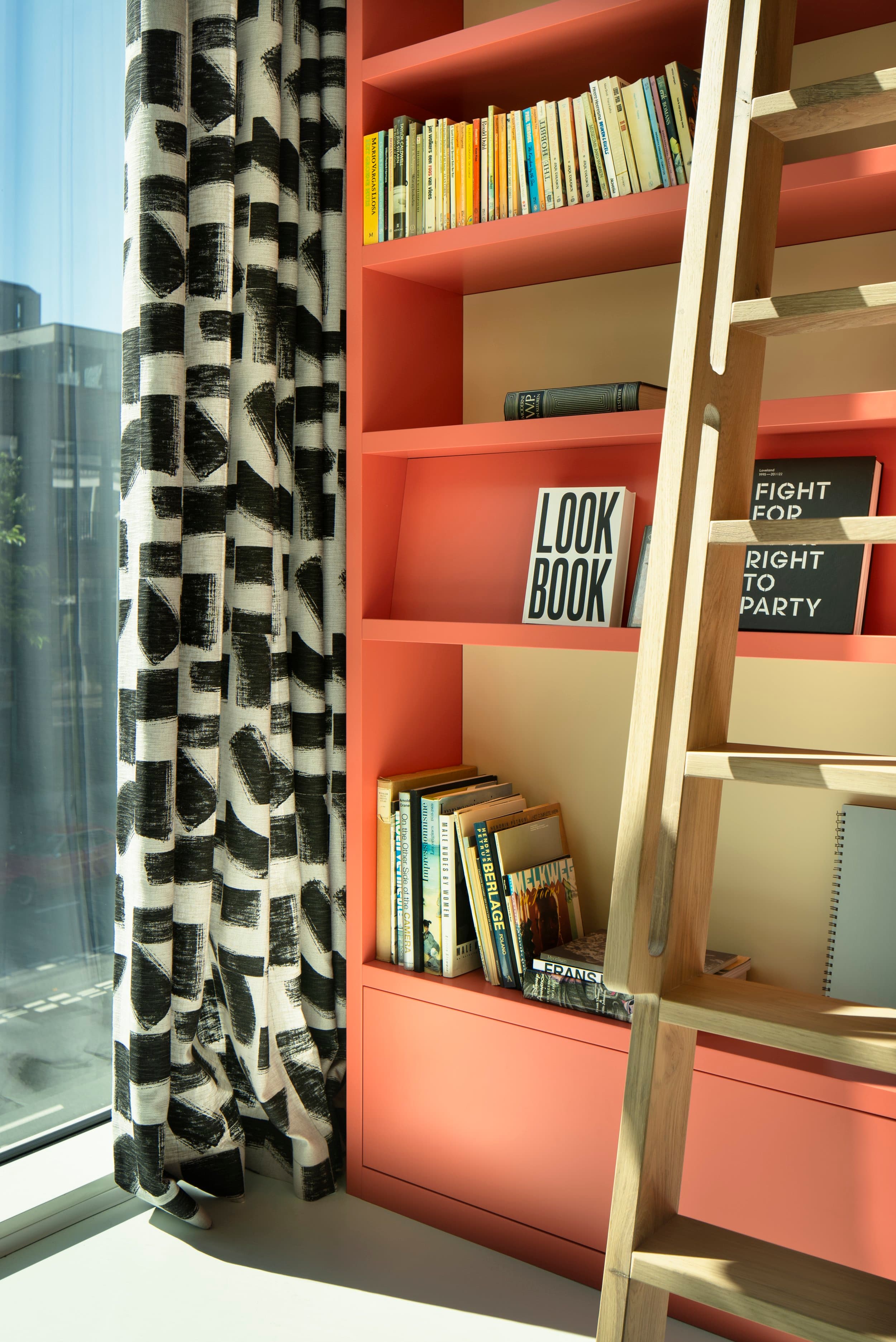 Boekenkast in rood staal met gekleurde boeken en open vakken