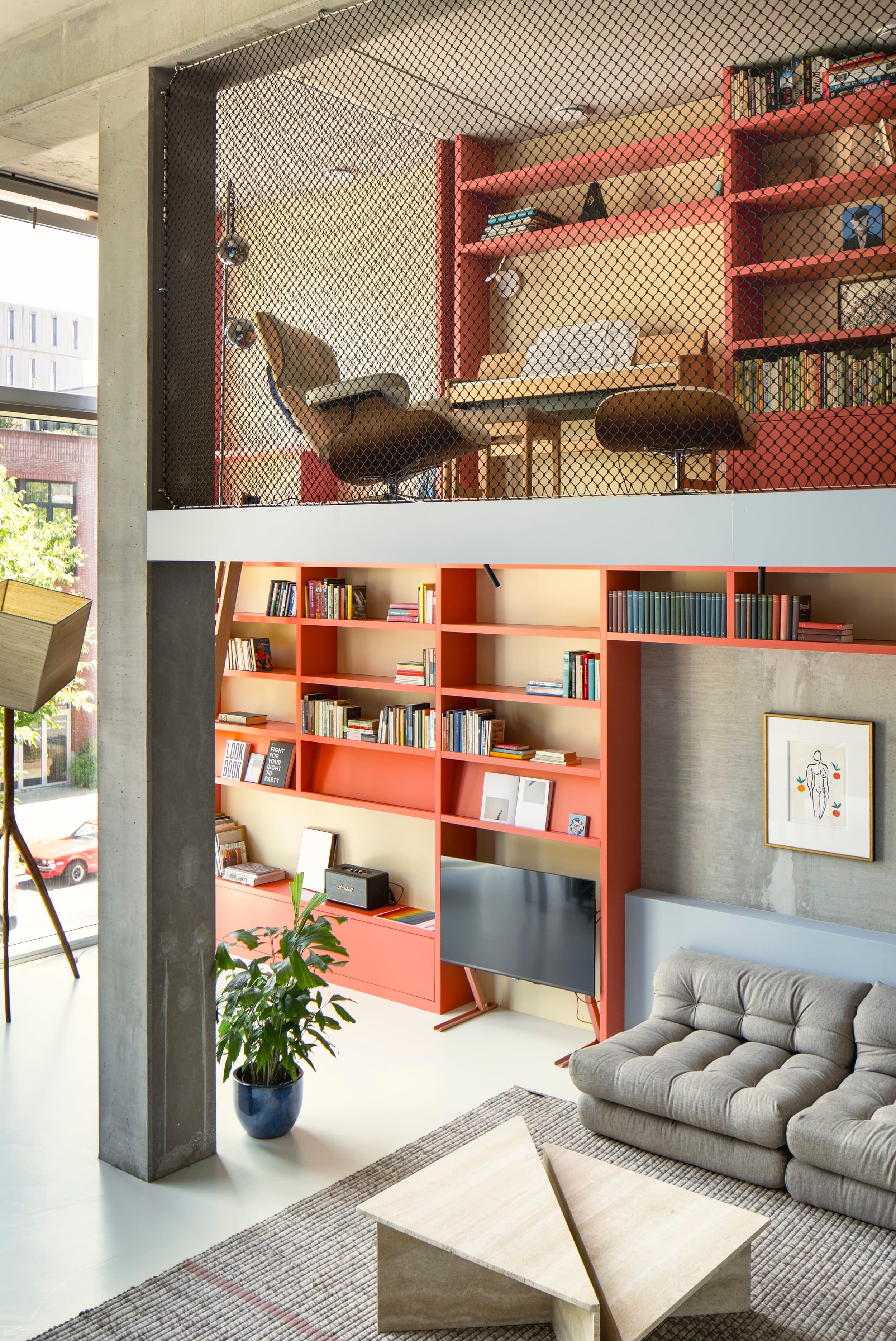 Woonkamer met rode stalen boekenkast, betonnen muur en grijze sofa