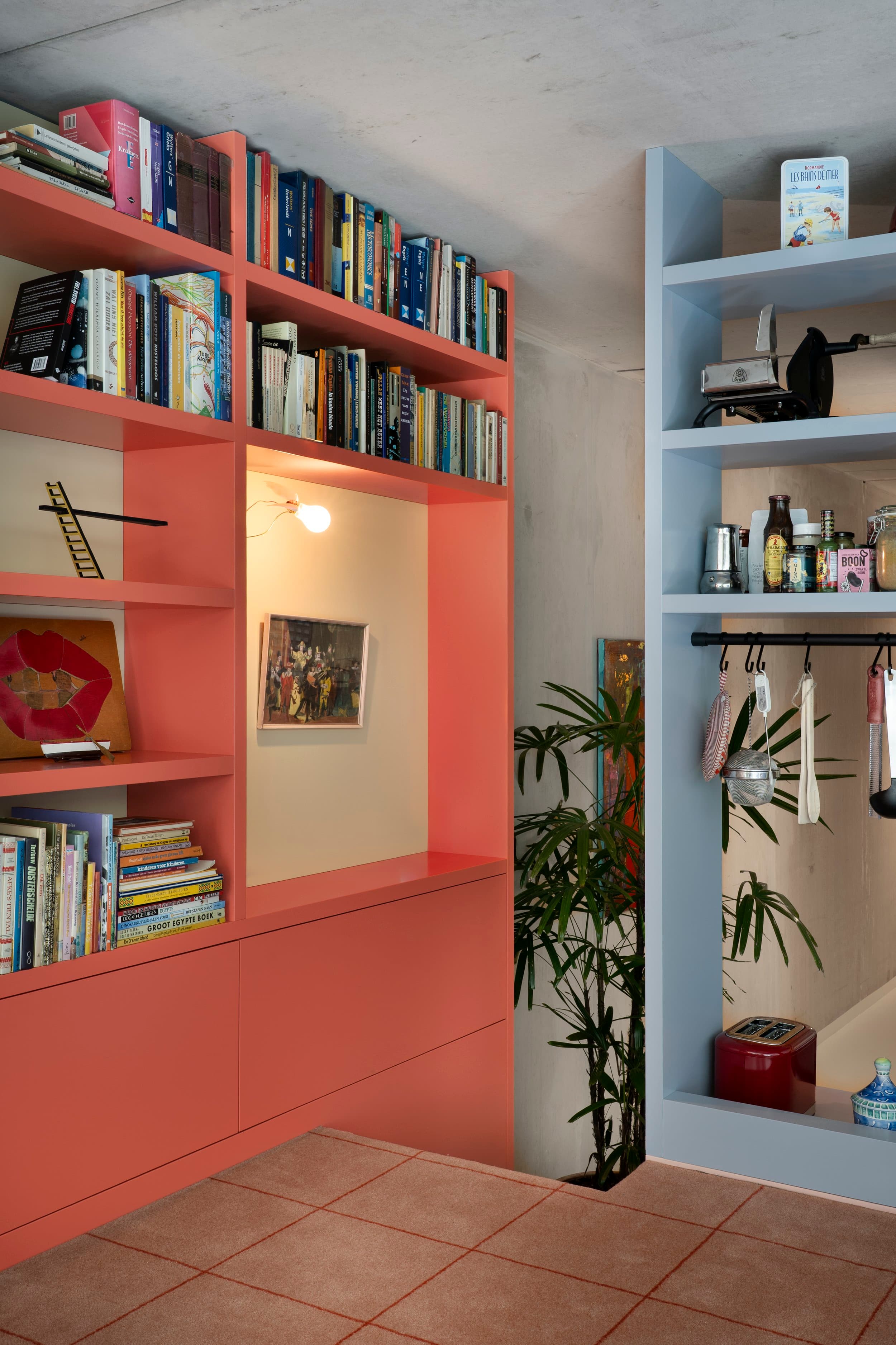 Rode stalen boekenkasten tegen betonnen muur met variabele vakken