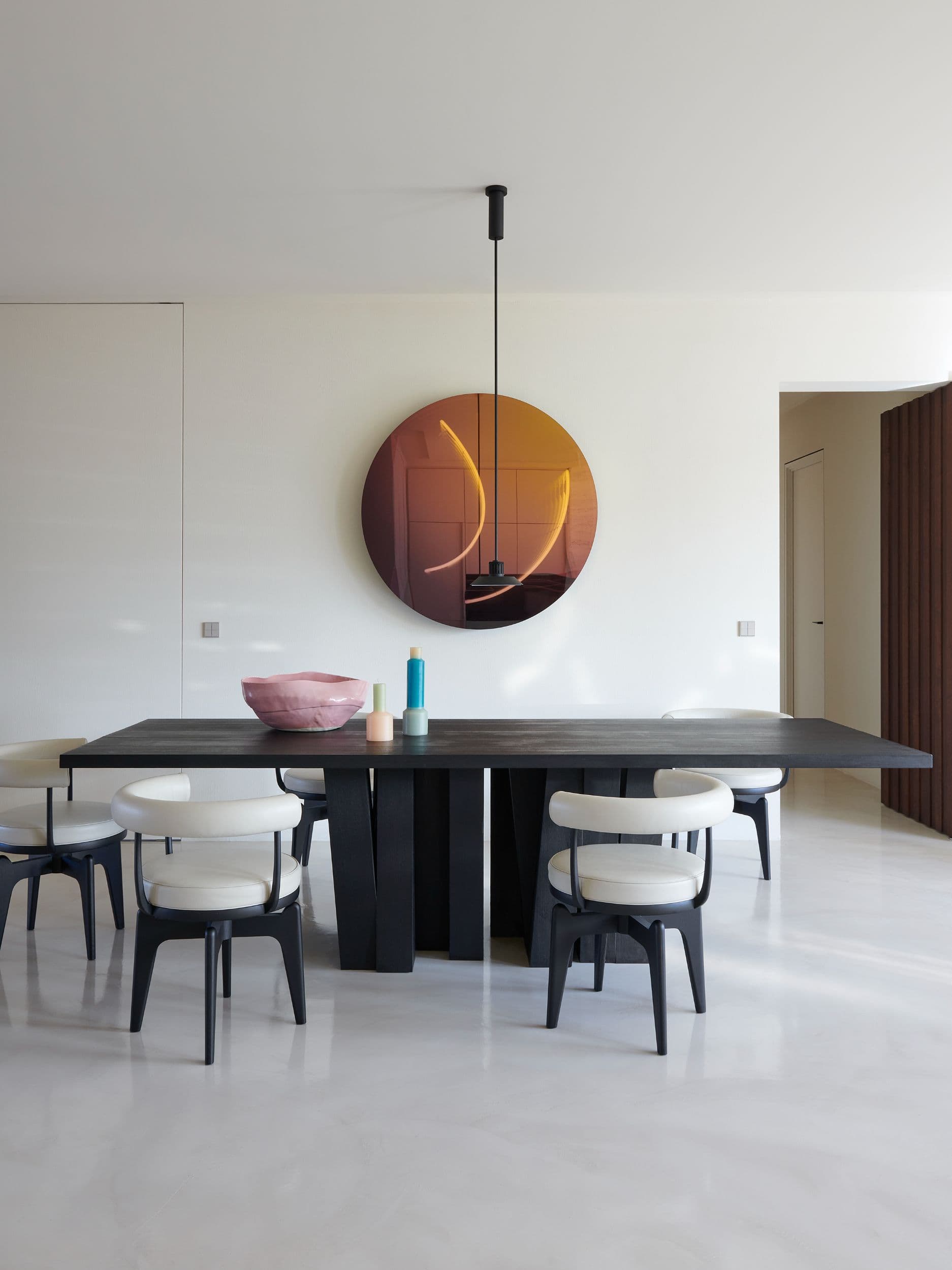 Eetkamer met zwarte eettafel, witte stoelen en ronde koperen wandlamp
