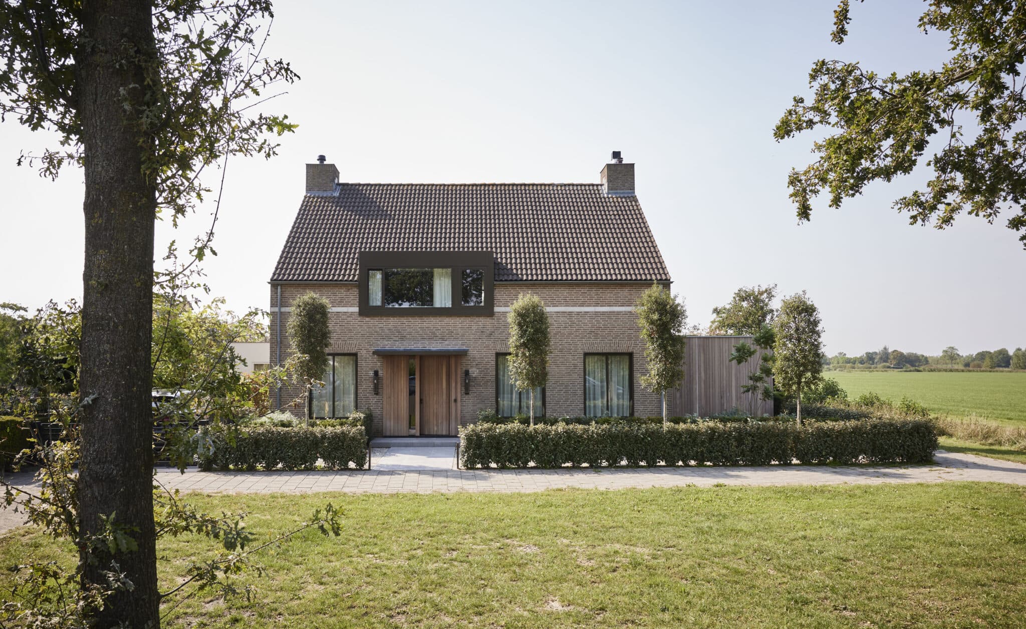 Bakstenen villa met pannendak en groene haagschermen langs oprit