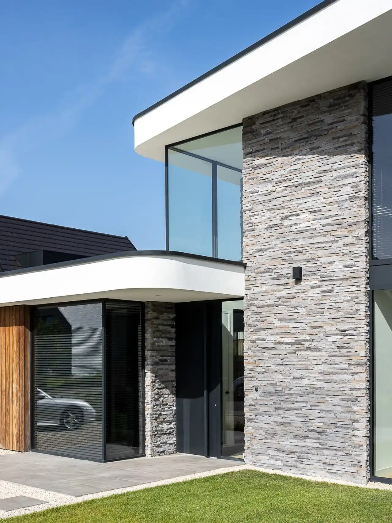 Hoekdetail gevel met natuurstenen wand, houten elementen en groene gazon