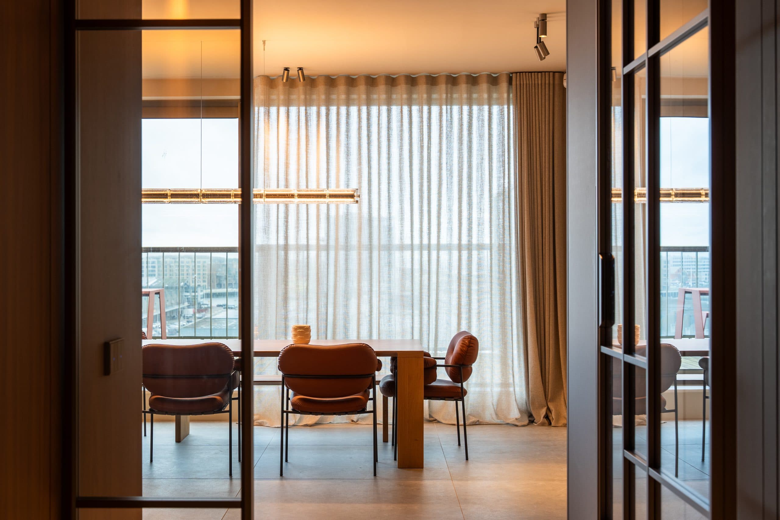 Slaapkamer met zithoek, terracotta stoelen en verticale textielgordijnen