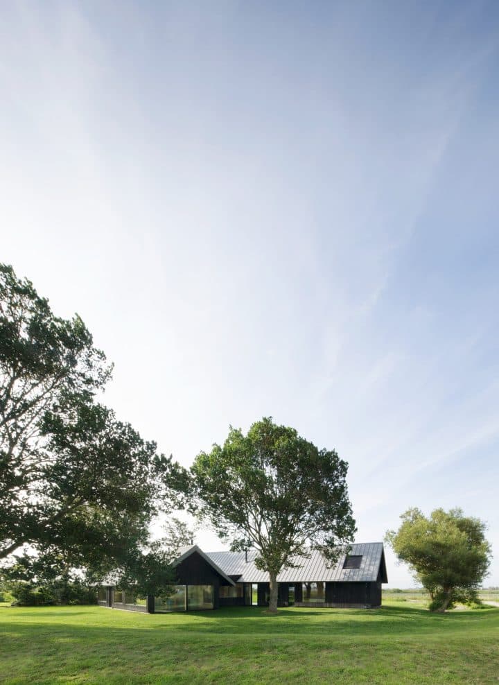 Zwarte moderne boerderij onder grote bomen in plat landschap