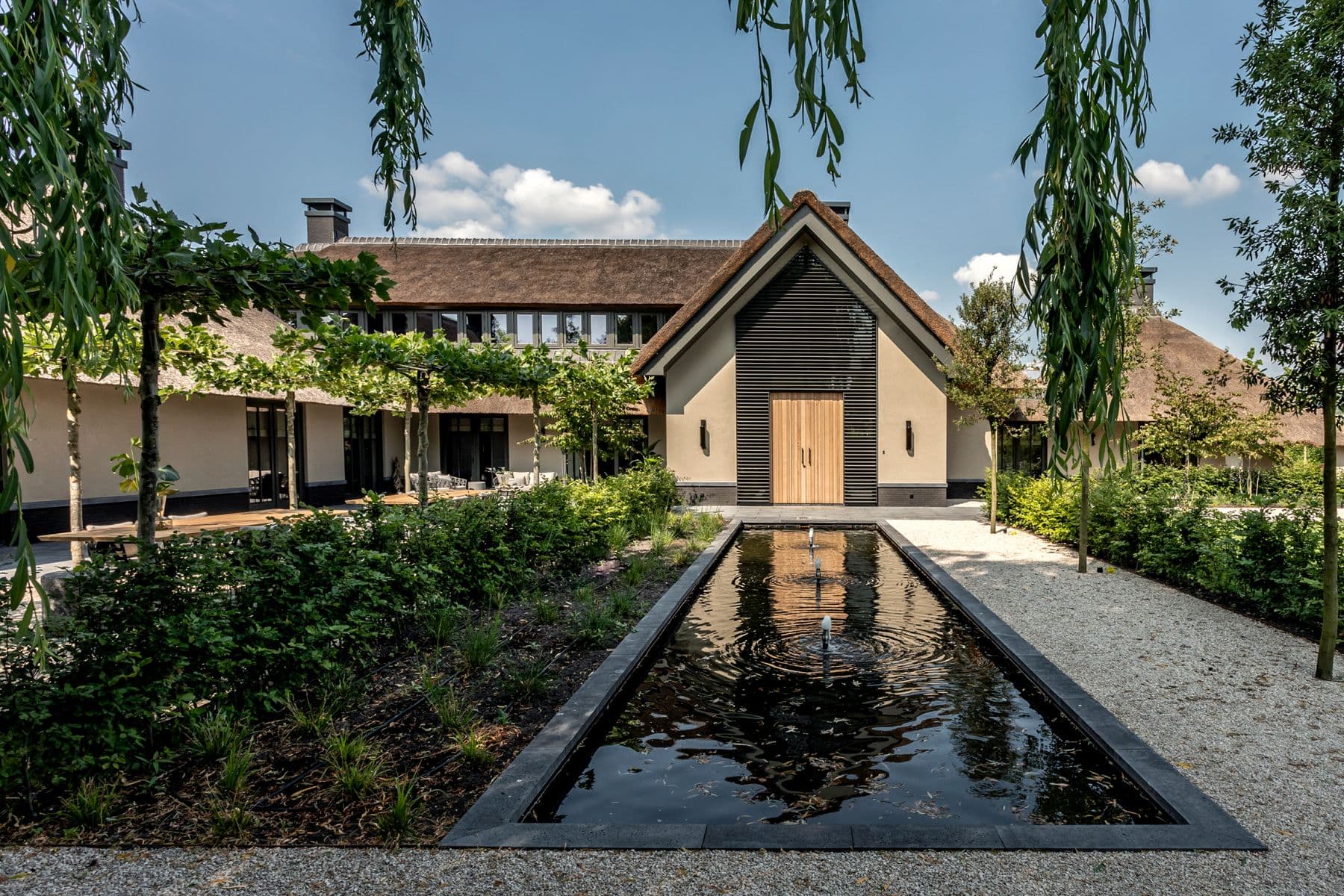 Rietgedekte villa met langwerpige waterpartij en grindpad
