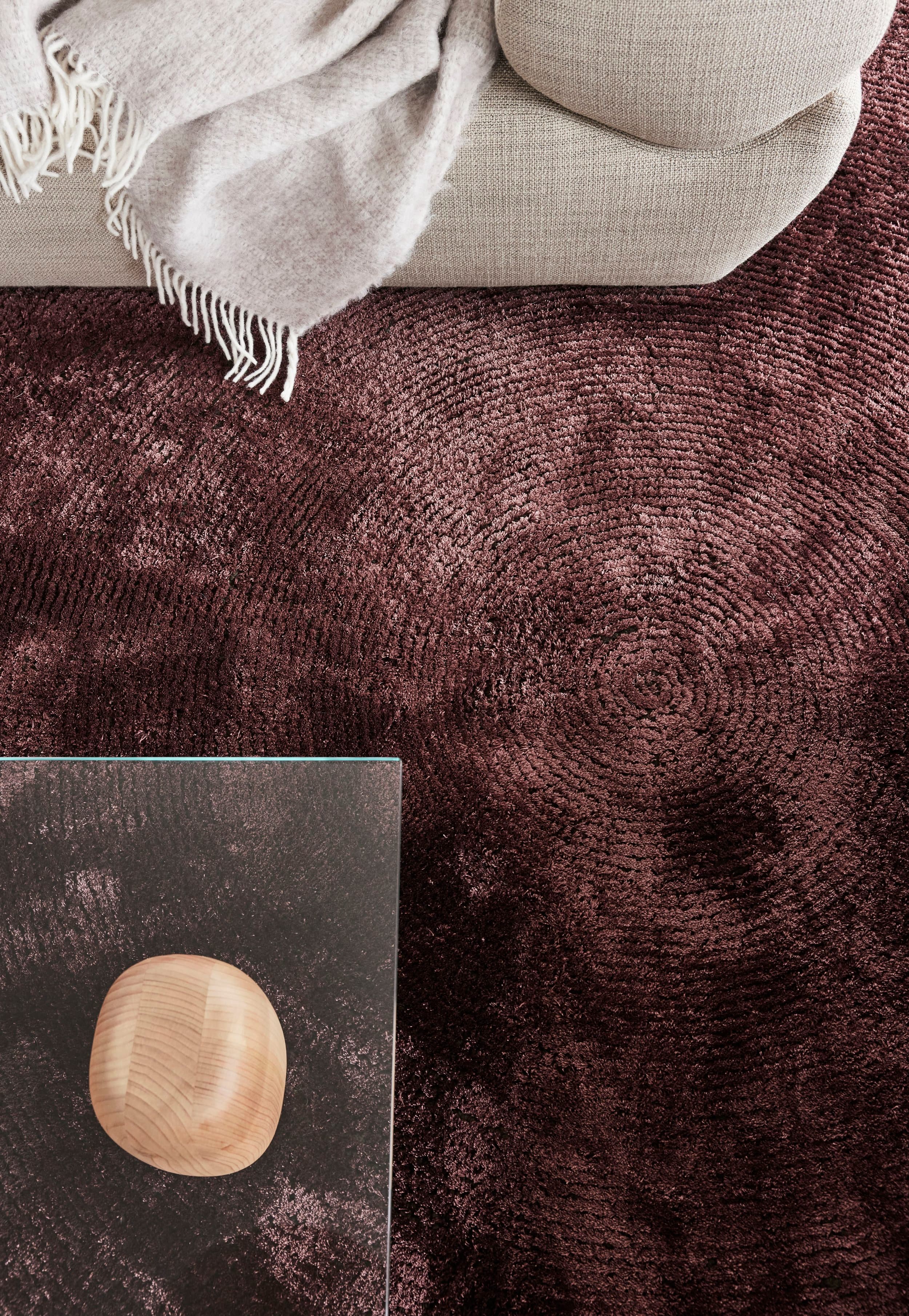 Detail aubergine vloerkleed met beige sofa en gebreide plaid