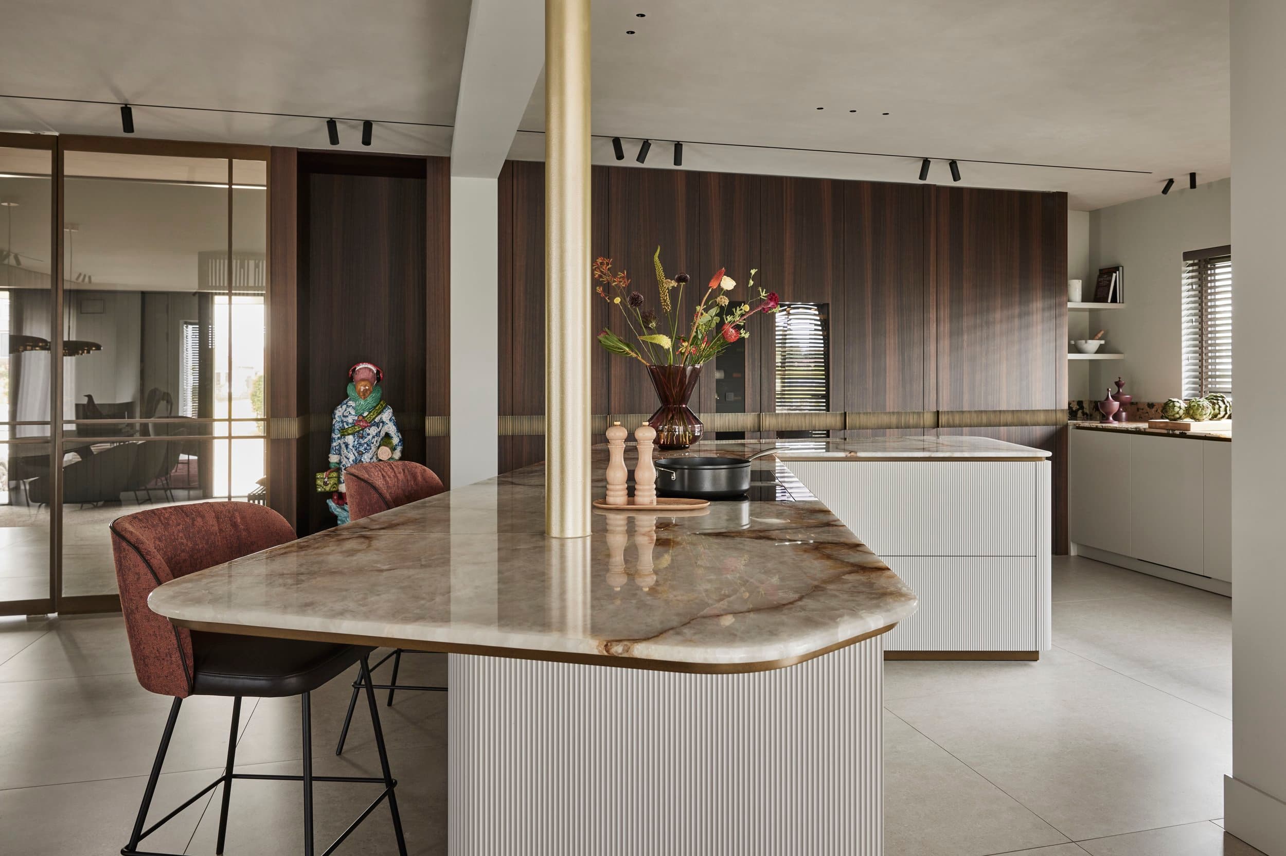 Open keuken met marmeren eiland, witte kasten en goud hanglamp