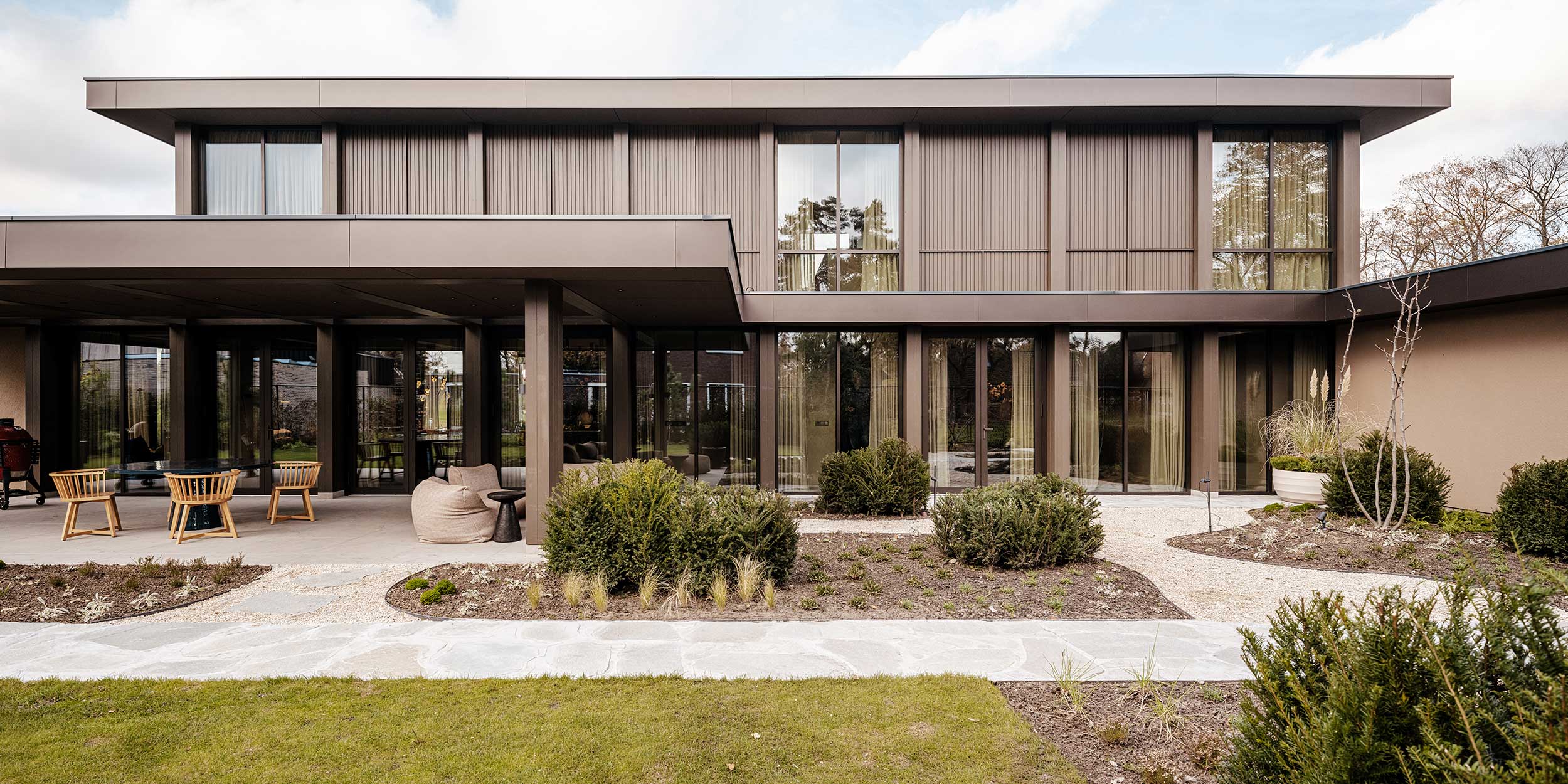Tuinzijde villa met terrasstenen en grote raampartijen, donkerbruine gevel