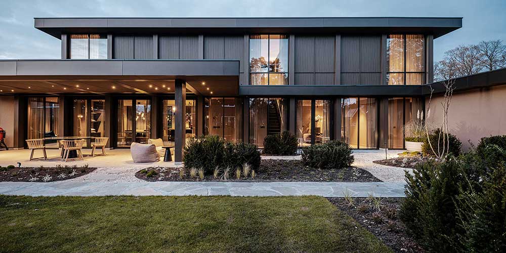 Tuinzijde villa met grijze baksteengevels en grote glazen schuifdeuren