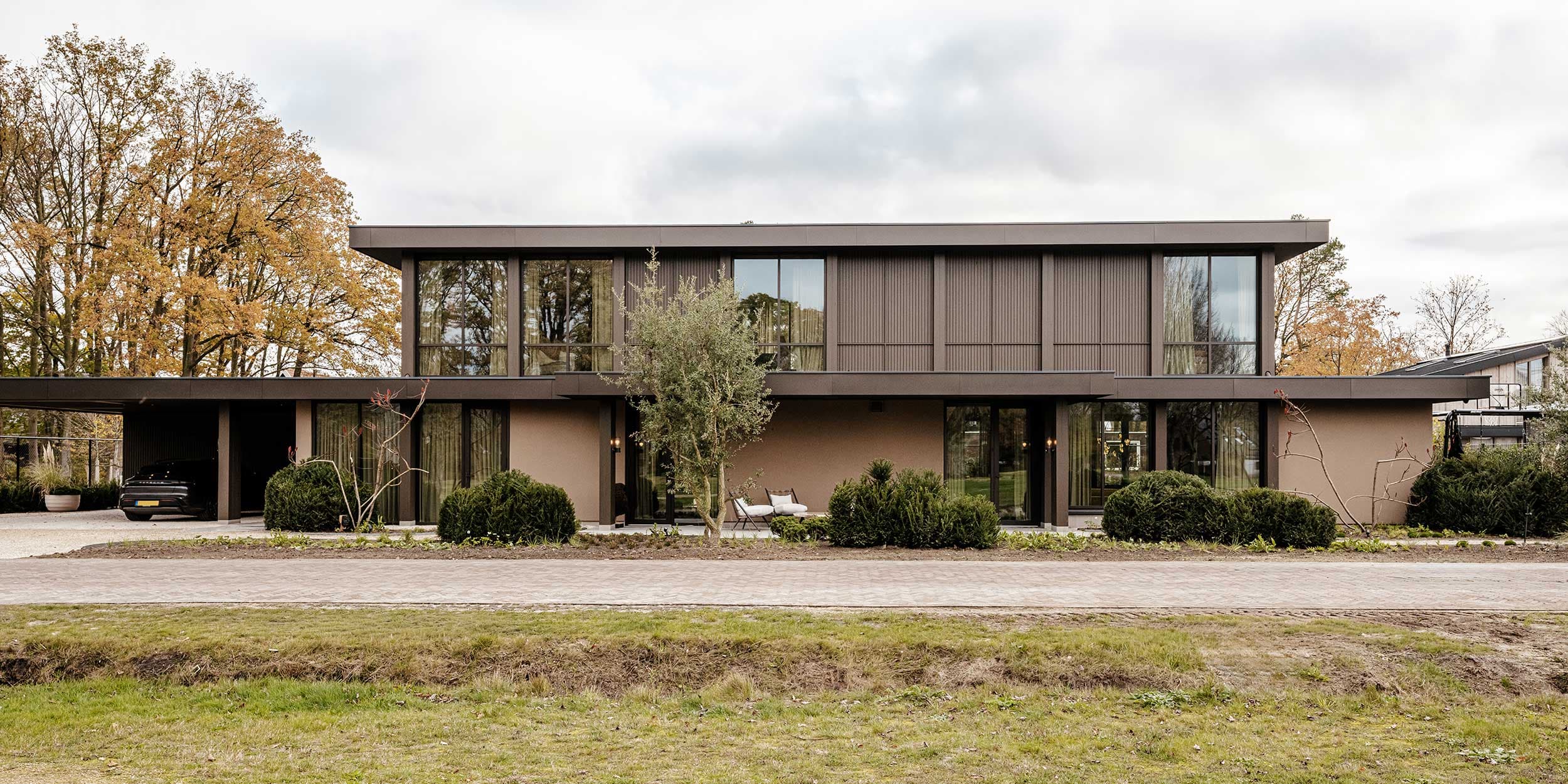 Tuinzijde met groot glazen schuifsysteem, terrasstenen en beige linnen zithoeken