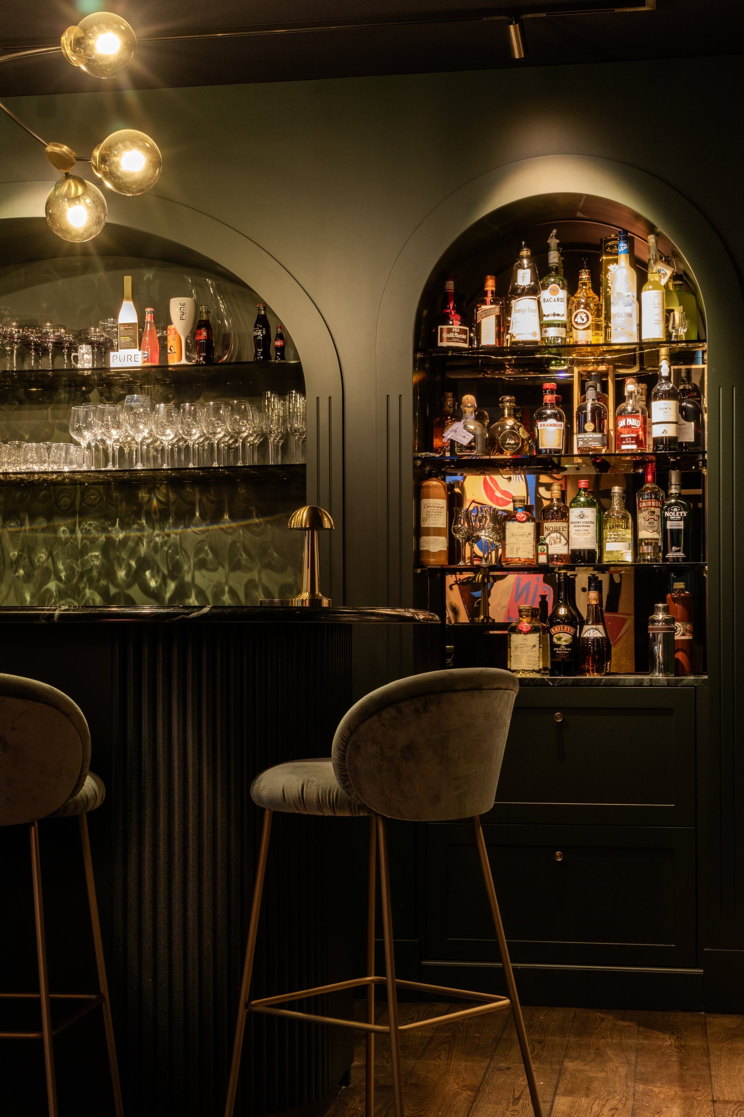 Sophisticated bar area with arched bottle display, moody lighting and upholstered seating